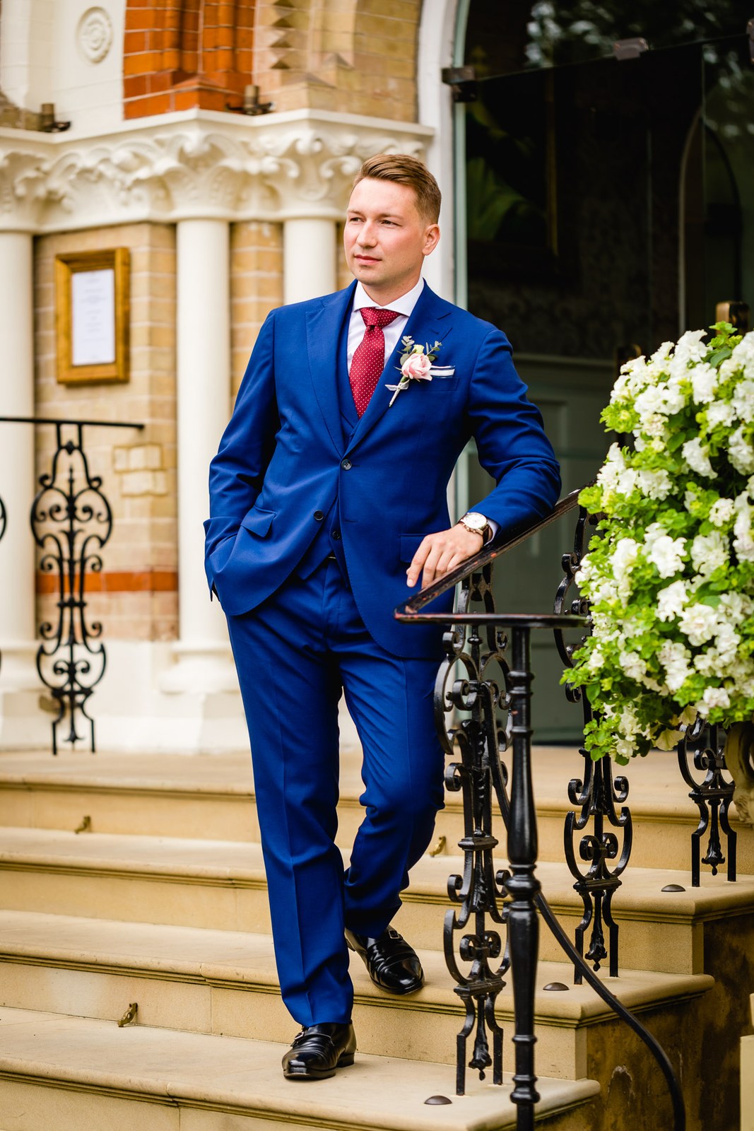 The groom in a blue suit descending the stone entrance steps of The Petersham Hotel