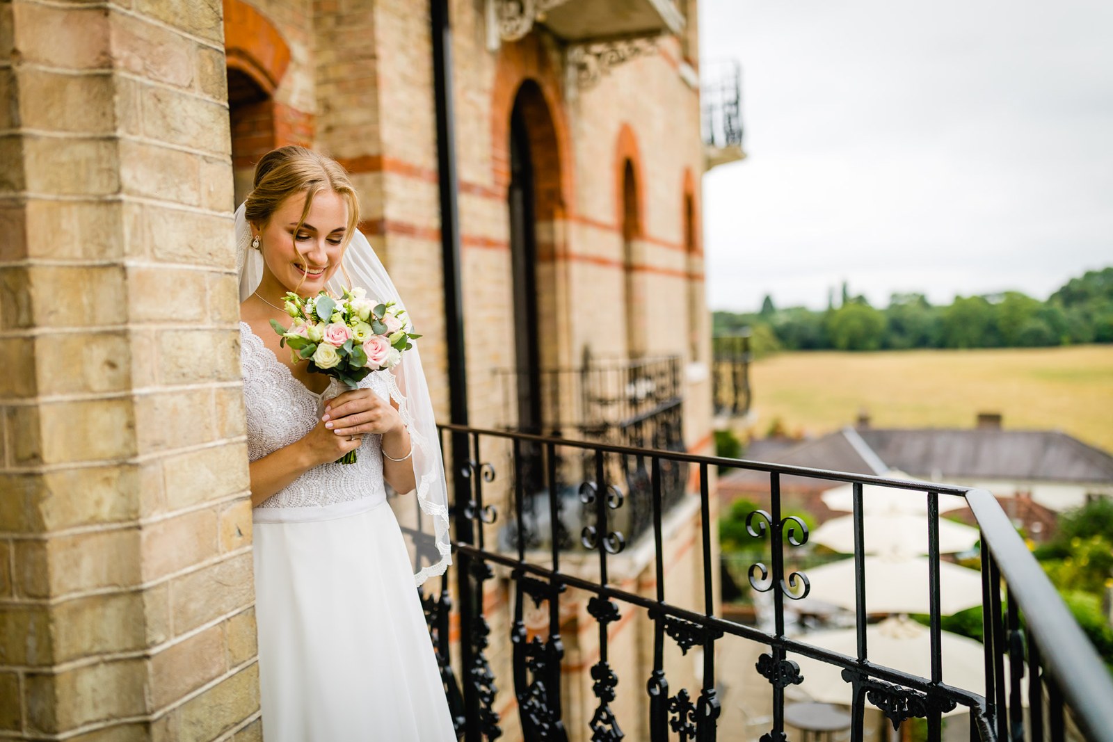 The bride on a balcony at The Petersham Hotel holding her bouquet, countryside beyond