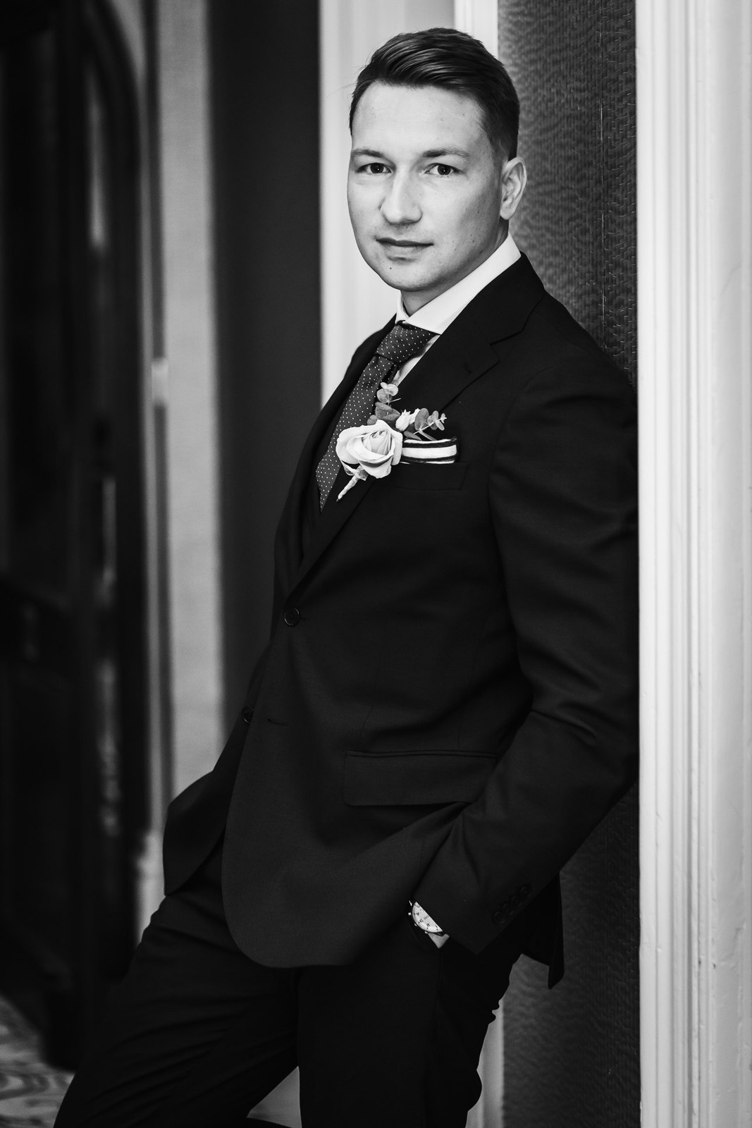 Black-and-white portrait of the groom leaning against a wall