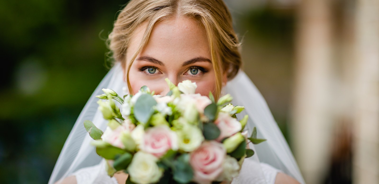 The bride peeking over her bouquet, her veil framing her face