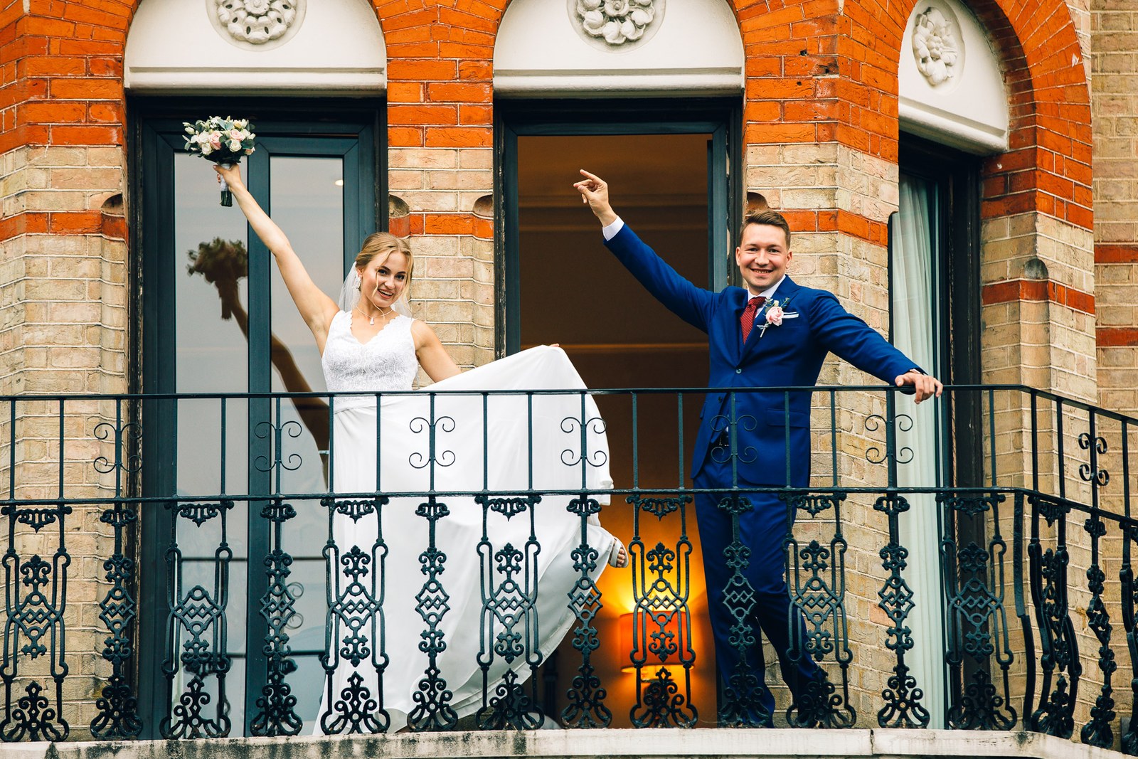 The newlyweds cheering from an arched brick balcony of The Petersham Hotel