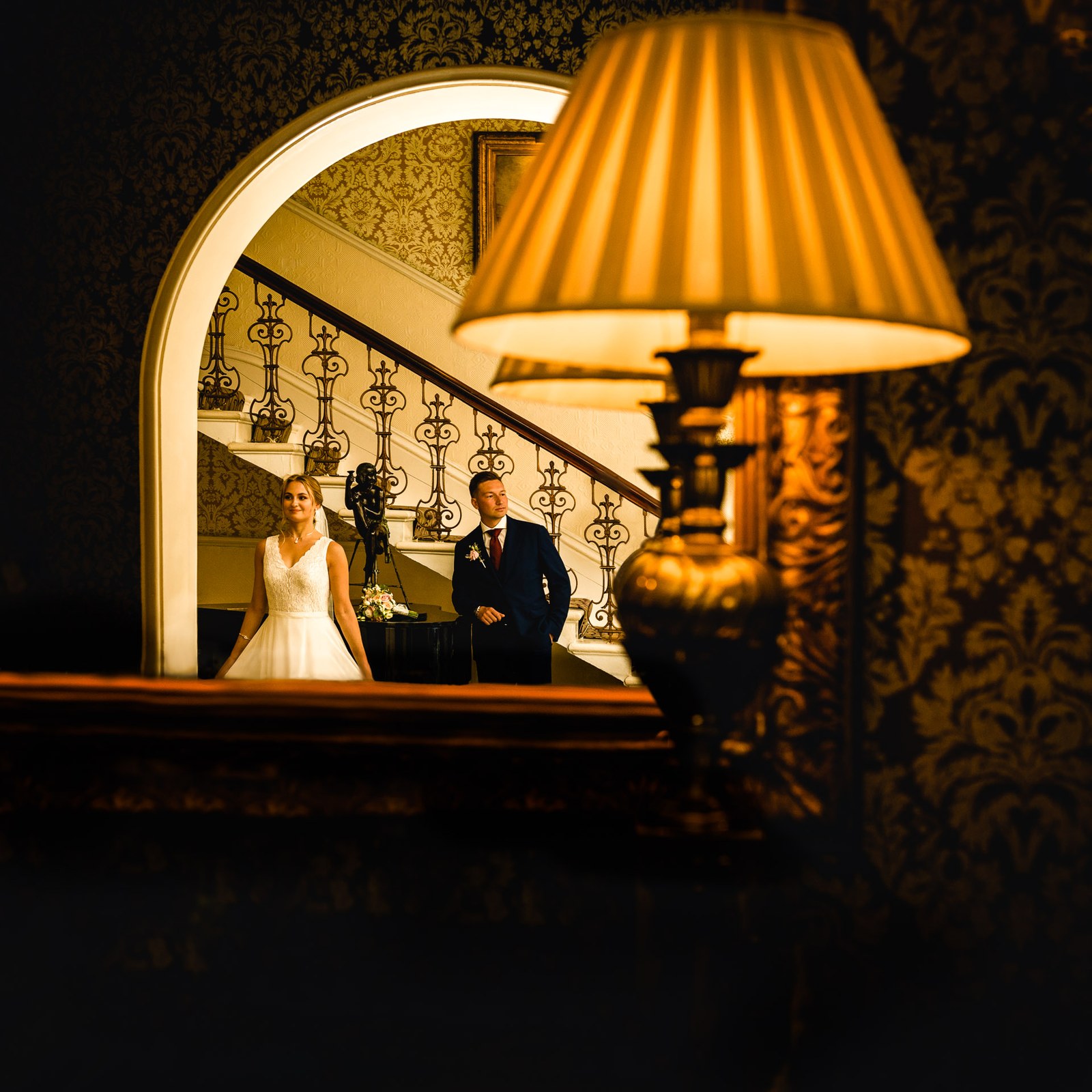 The couple reflected in a mirror on the staircase, a warm table lamp in the foreground