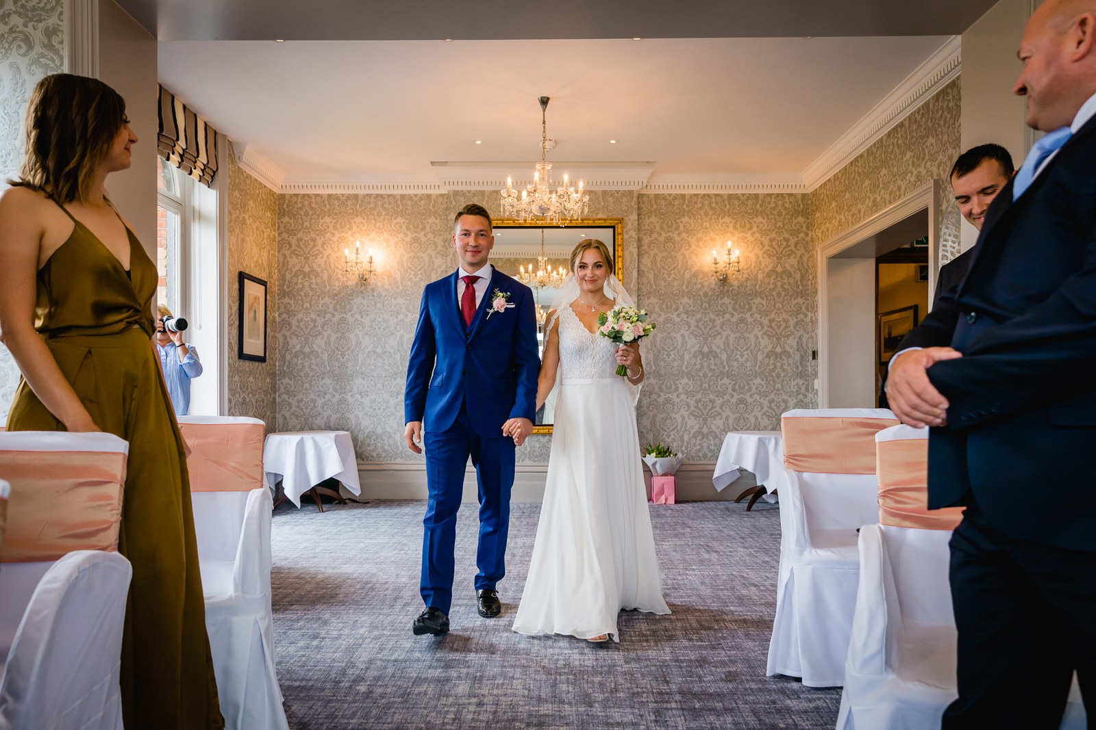 The couple entering a reception room at The Petersham Hotel beneath a chandelier