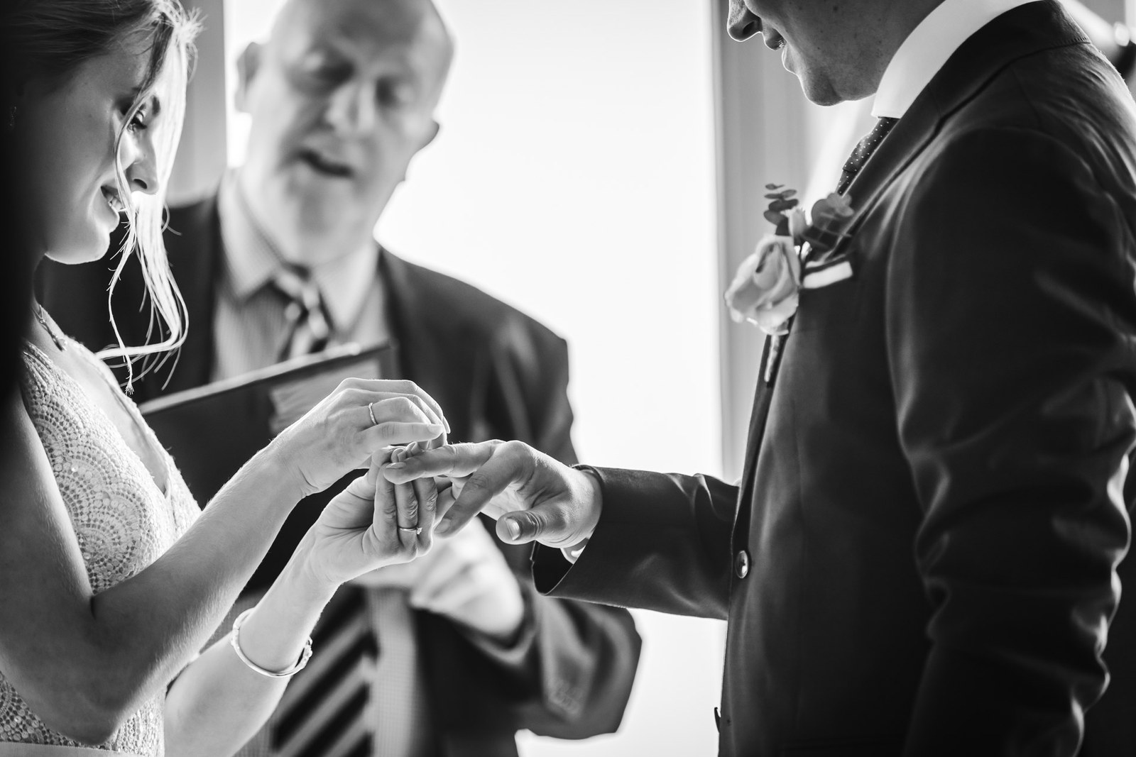 Black-and-white shot of the bride placing a ring on the groom's hand