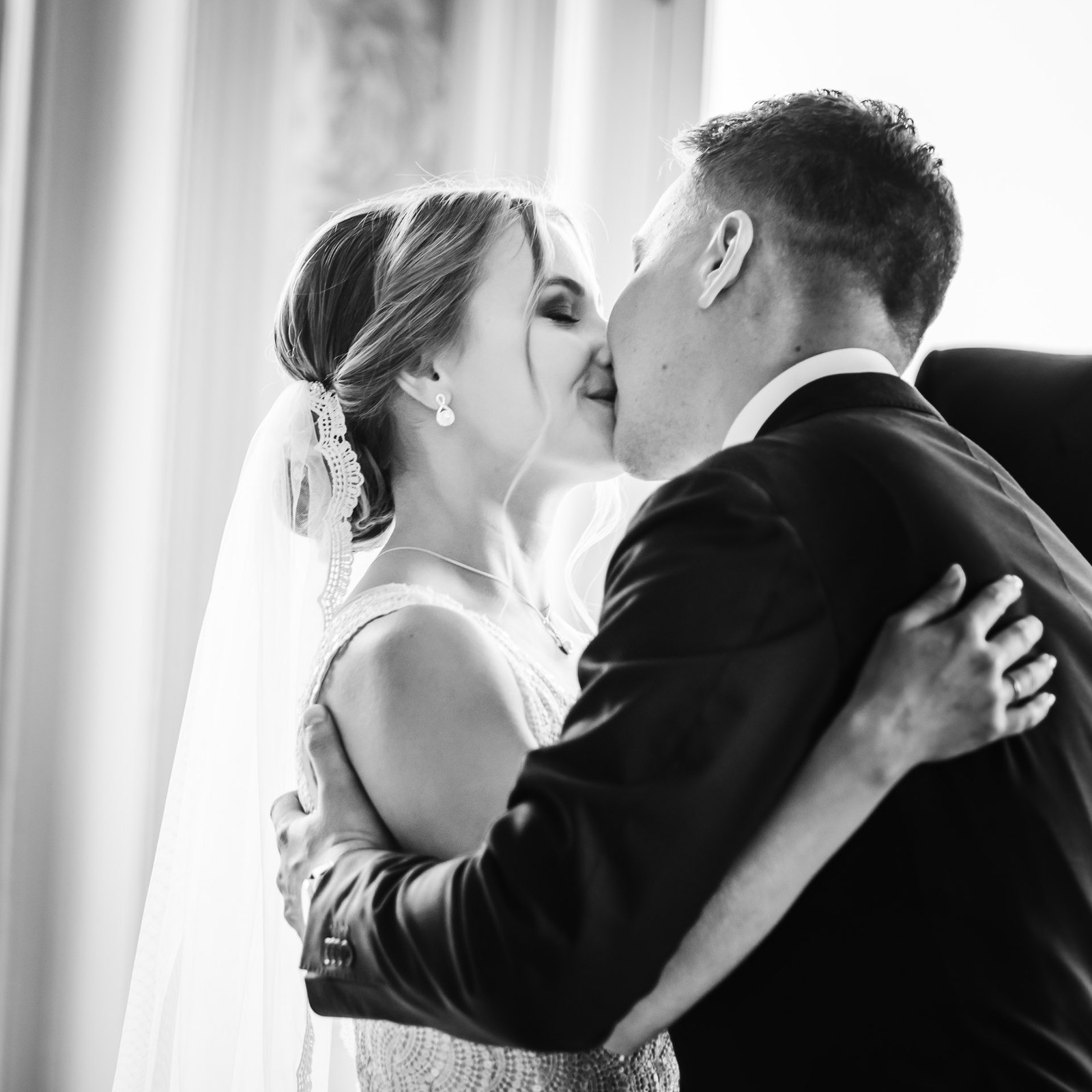 Black-and-white first kiss beside a curtained window