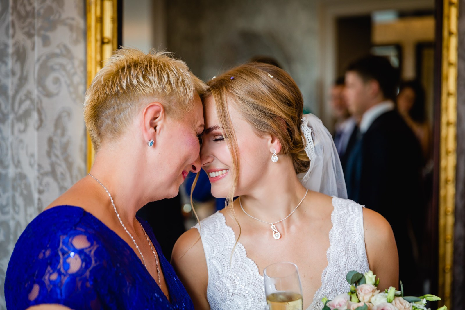 The bride resting her head against a woman in a blue lace dress