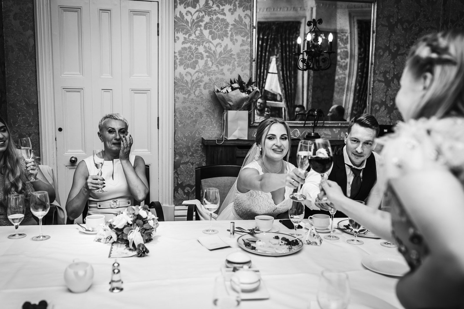 Black-and-white shot of the couple toasting with guests at dinner