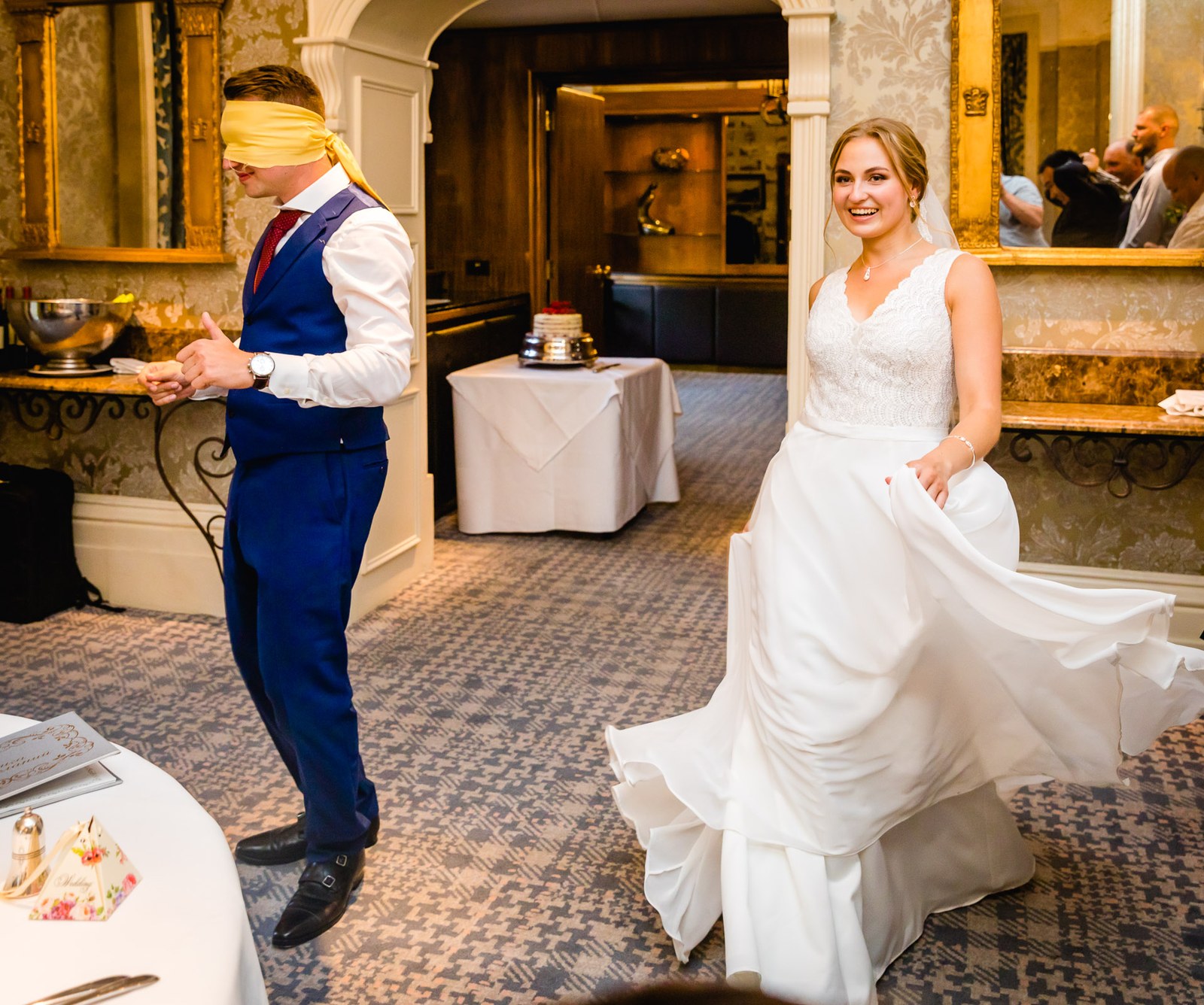 The blindfolded groom guessing during a game as the bride lifts her hem