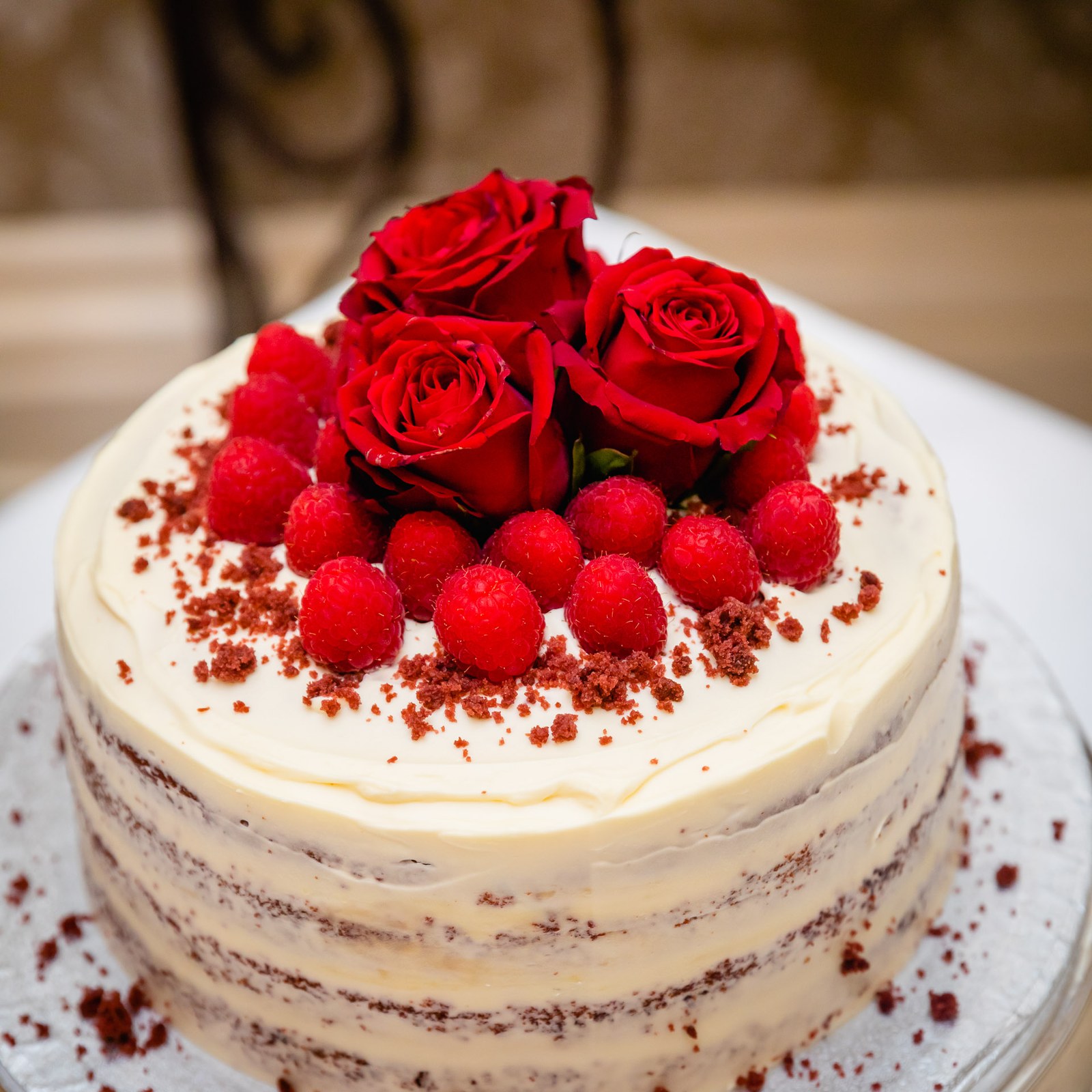 A red velvet naked cake topped with red roses and raspberries