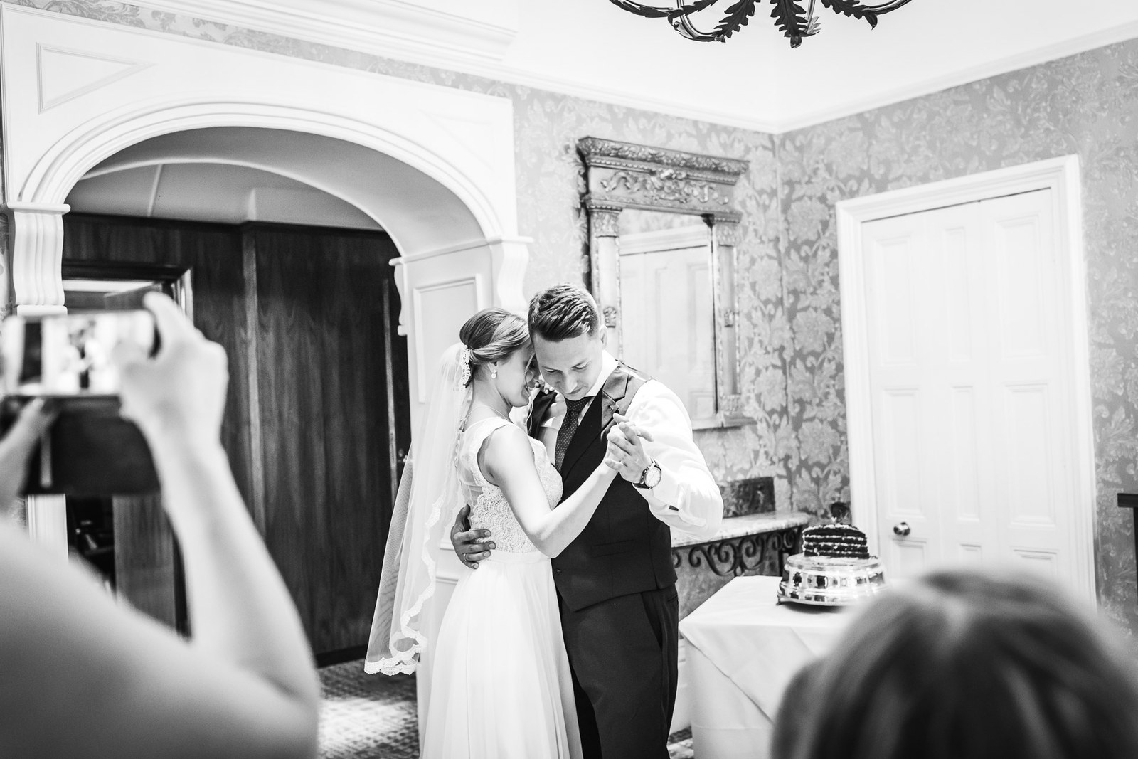 The couple's first dance as a guest films them, the cake behind
