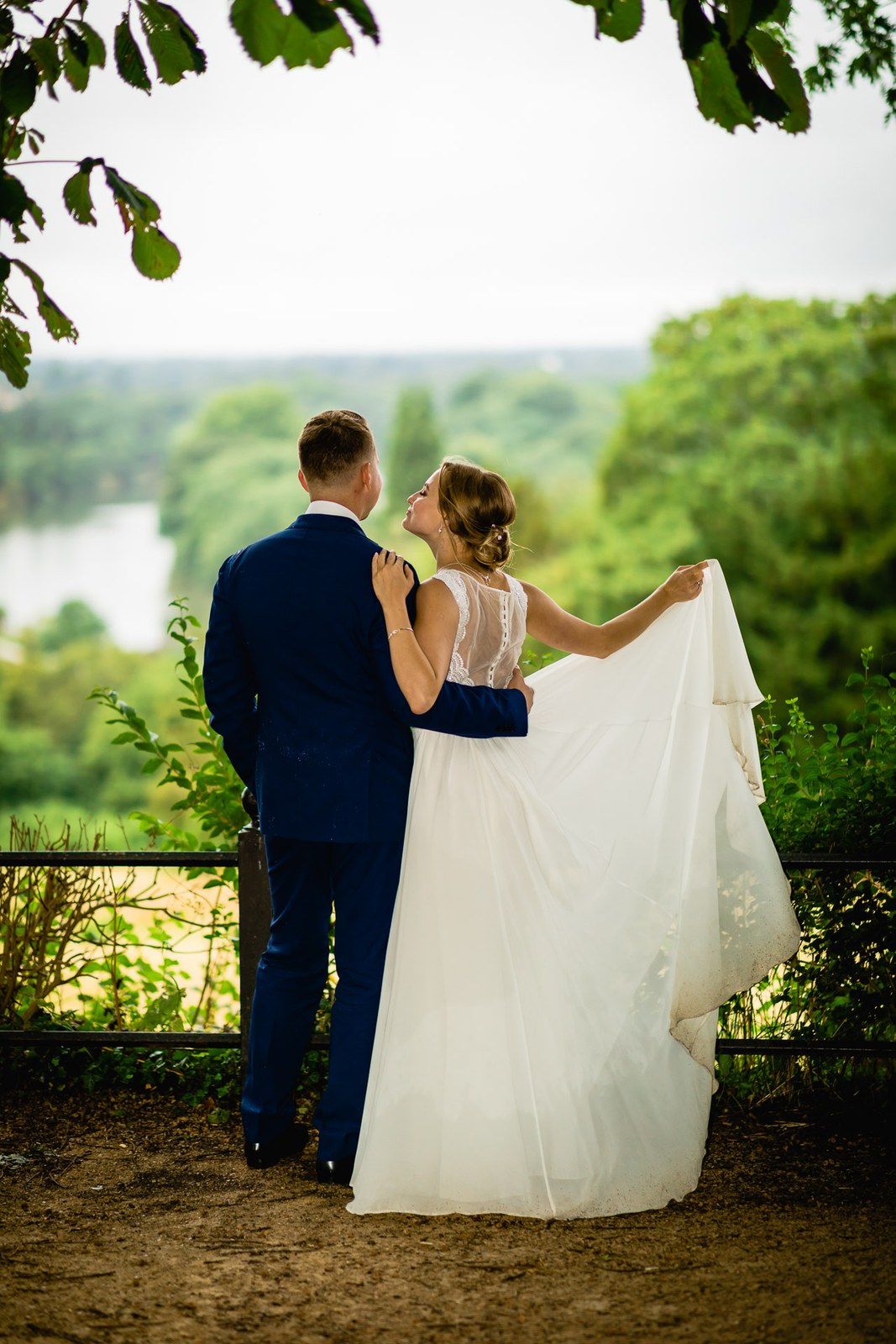 The couple admiring the river view, the bride holding out her gown