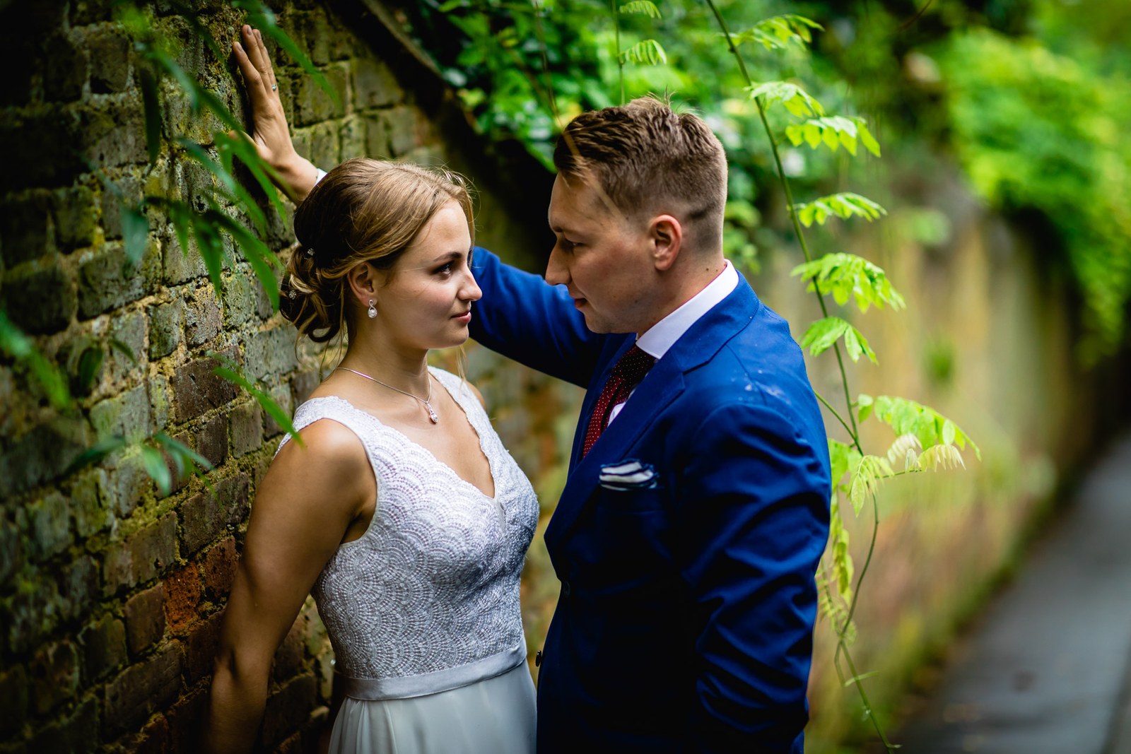 The couple by an old brick wall framed by greenery