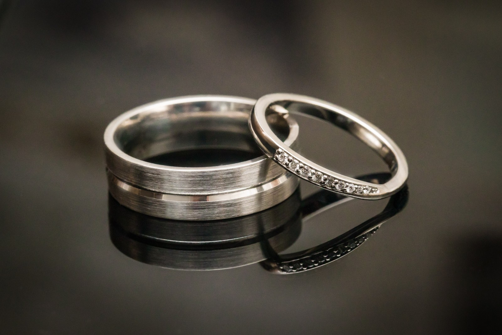 The two wedding rings, a plain band and a diamond band, on a dark surface