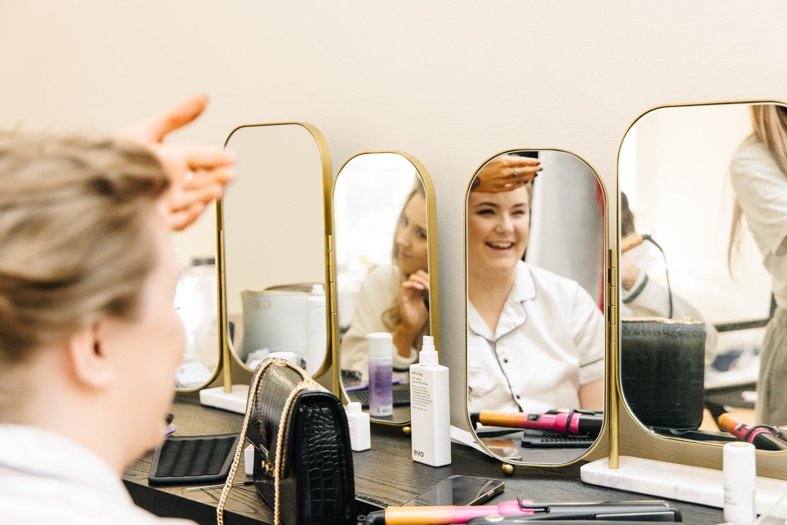 A bridesmaid at the lit dressing-table mirrors during hair and makeup