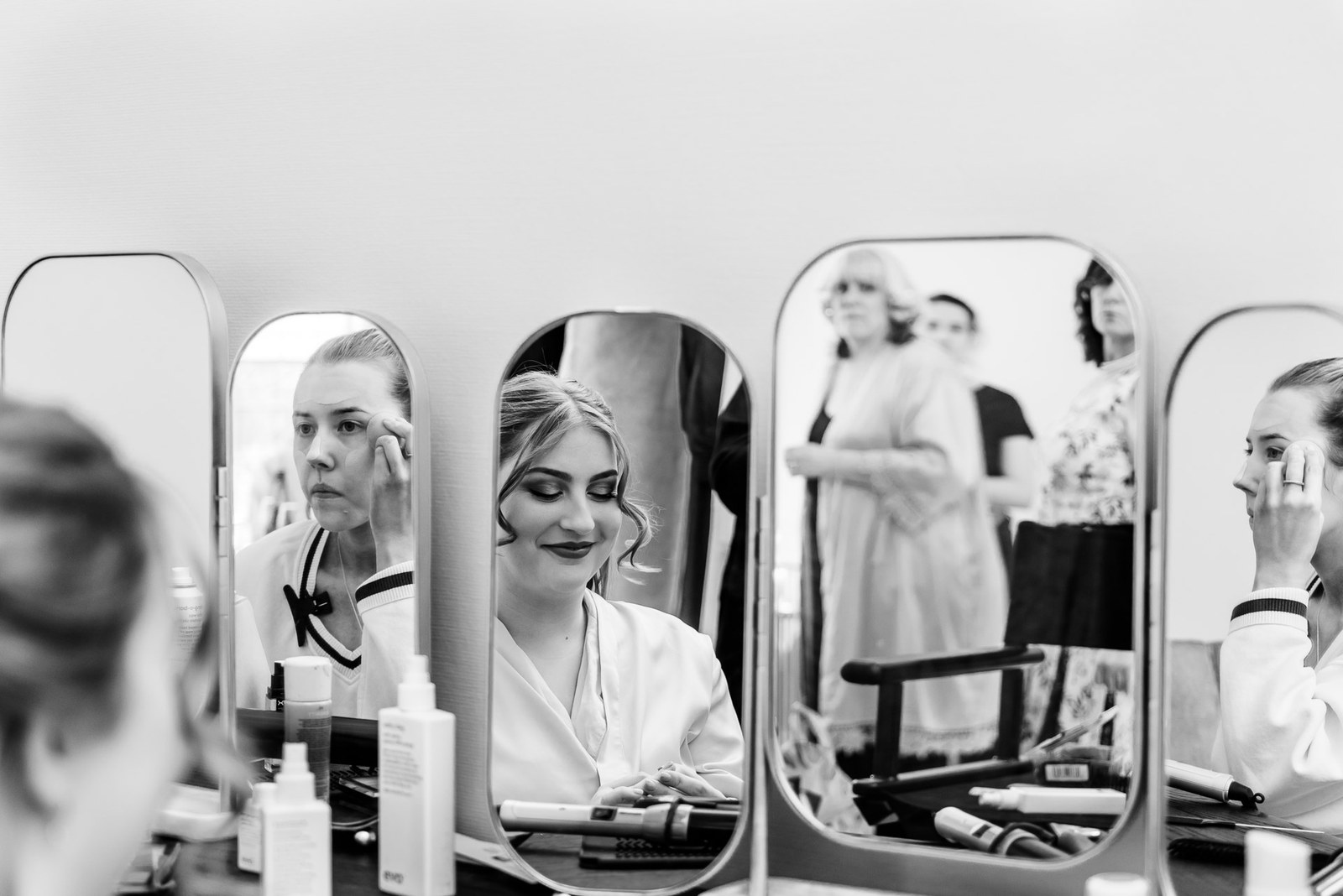 Black-and-white shot of the bride and bridesmaids getting ready at the vanity mirrors
