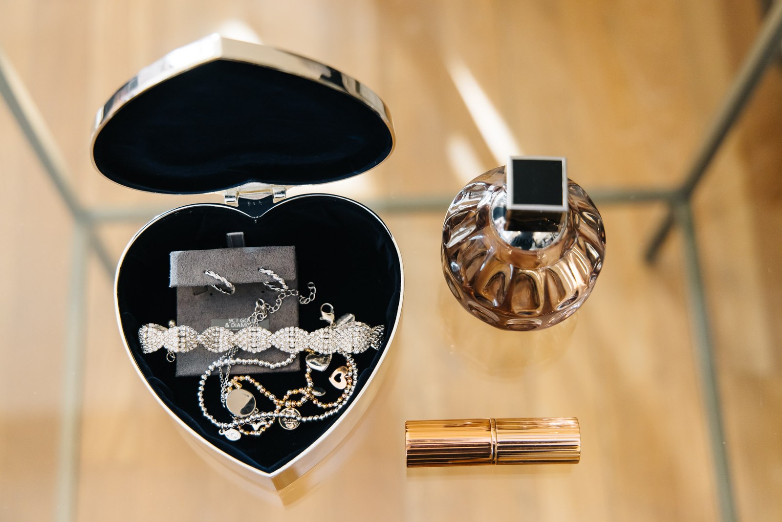 An open heart-shaped jewellery box with a bracelet, perfume and lipstick