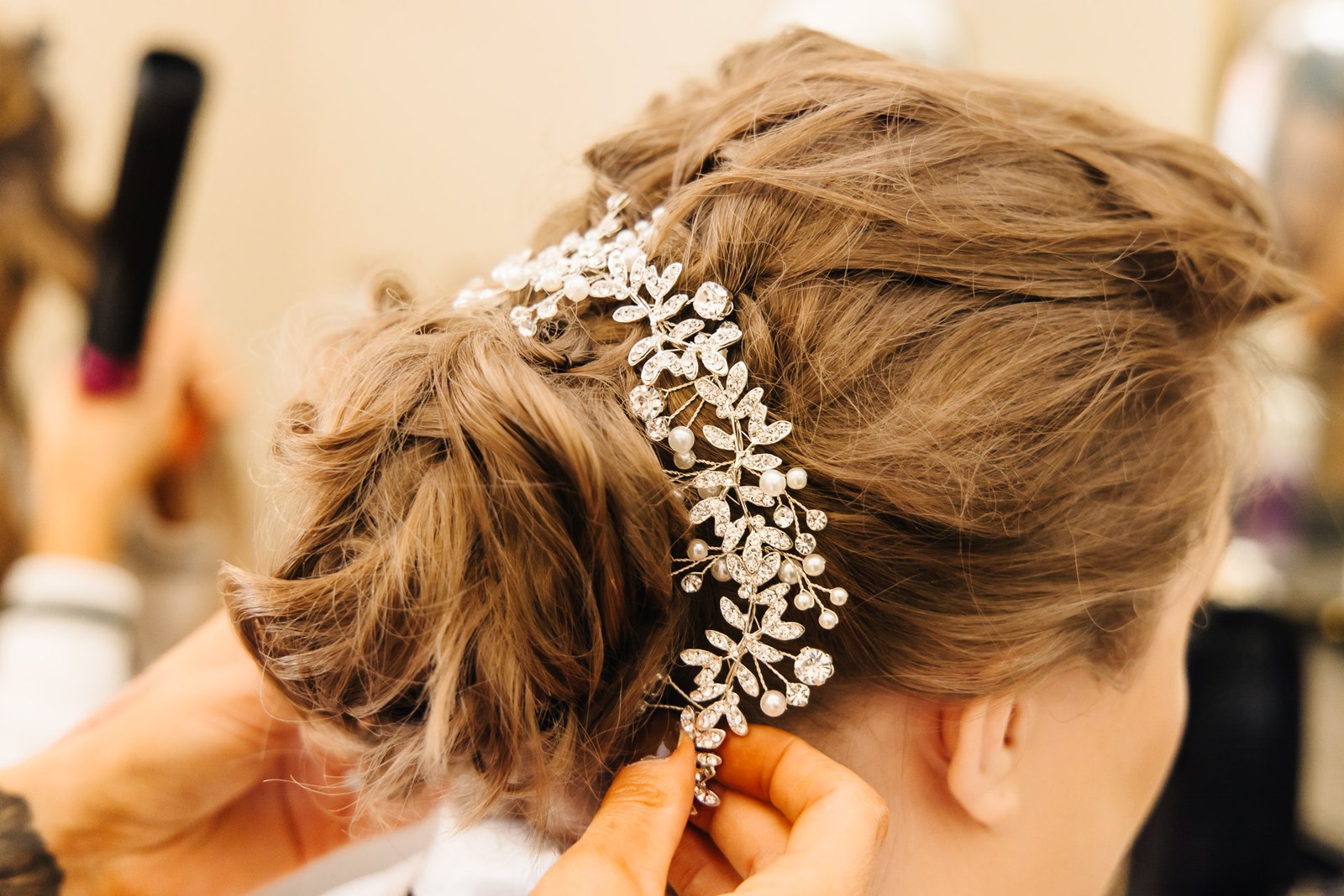 Close-up of a stylist fixing a crystal hairpiece into the bride's updo