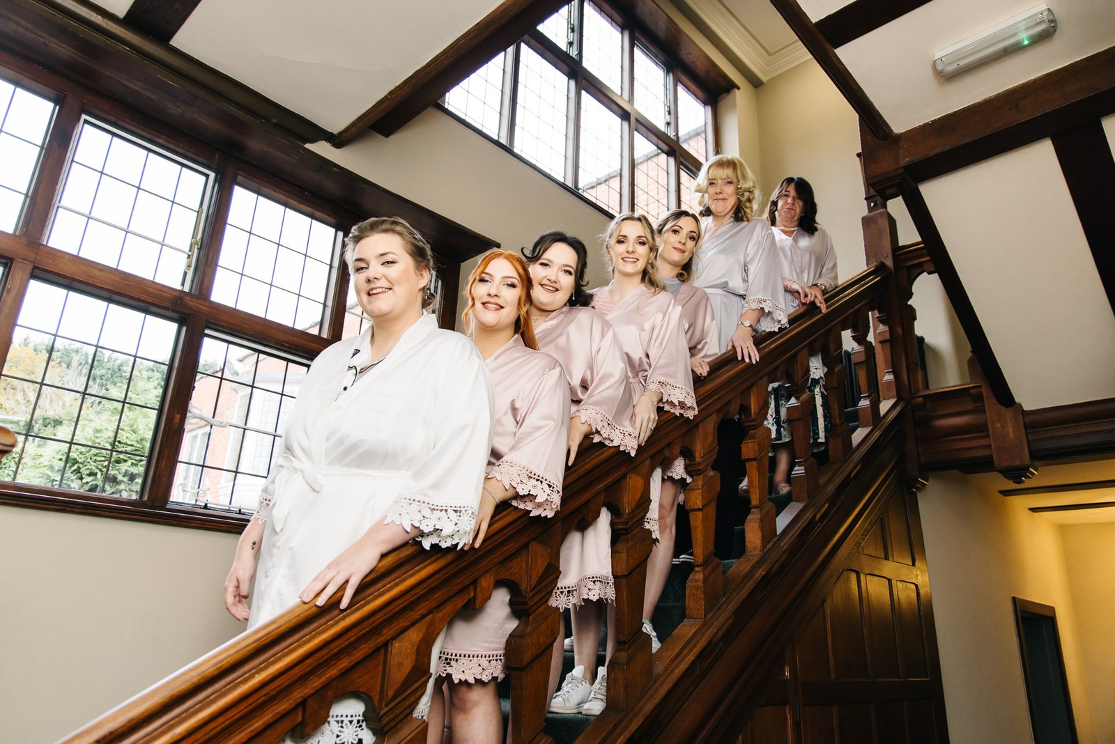 The bride and bridesmaids posing on a wooden staircase with leaded windows