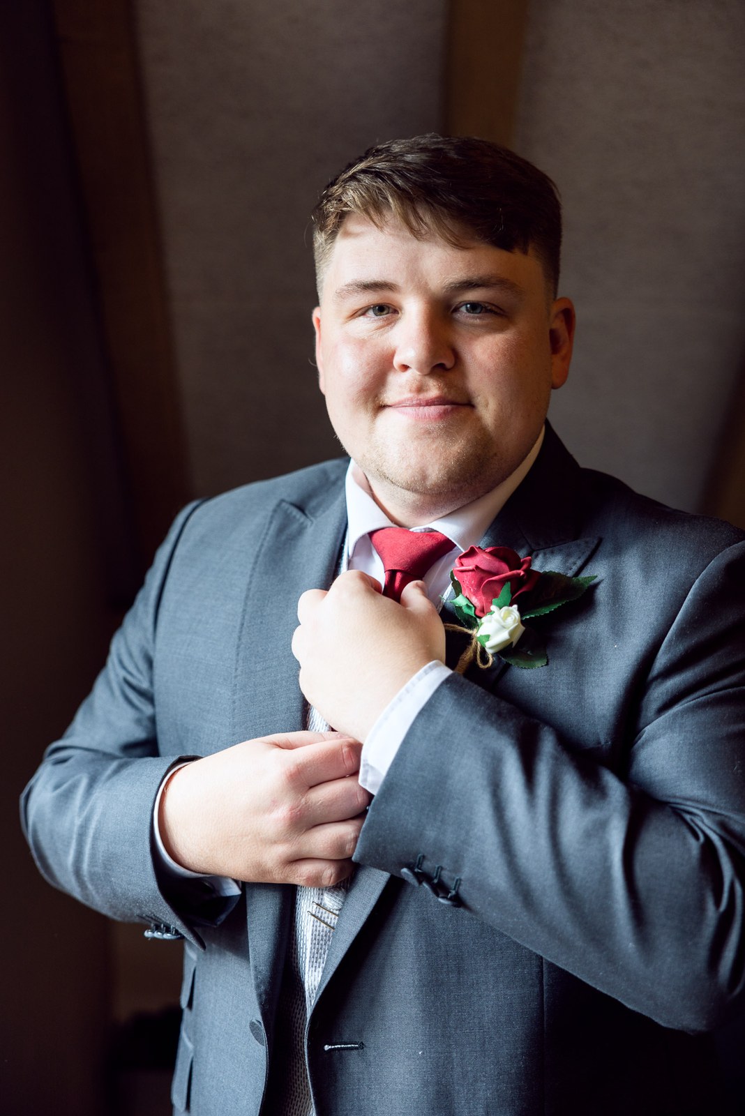 The groom in a grey suit straightening his red tie