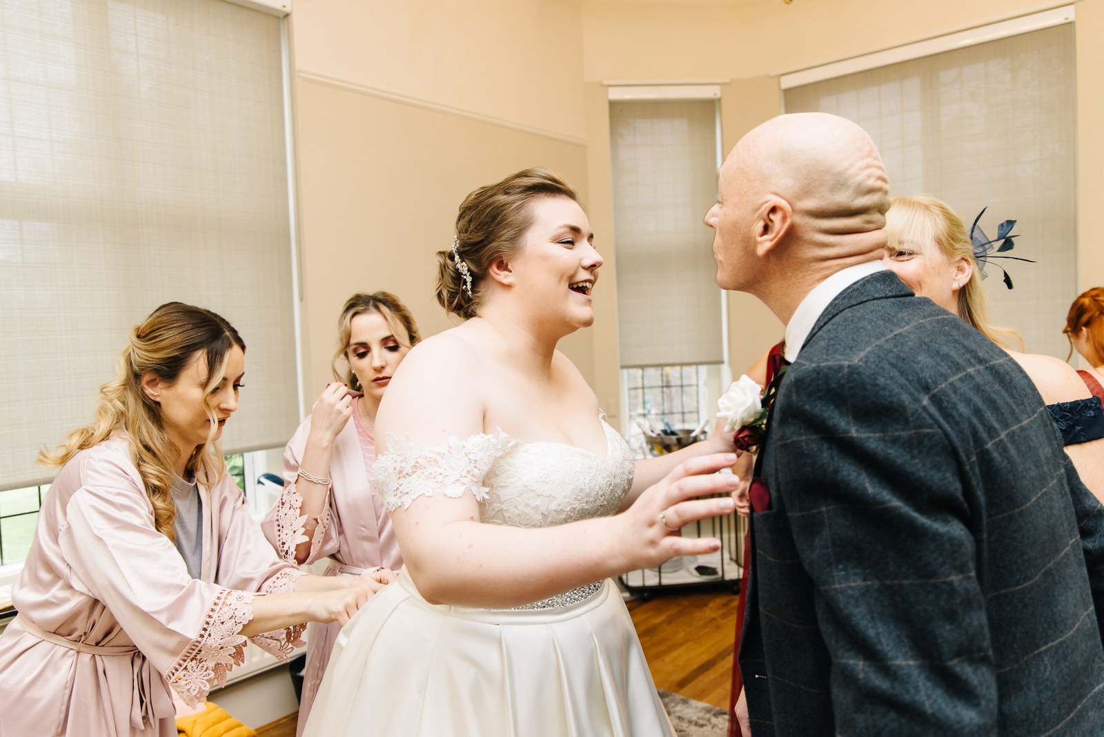 The bride laughing as she pins a buttonhole on a guest, bridesmaids gathered round