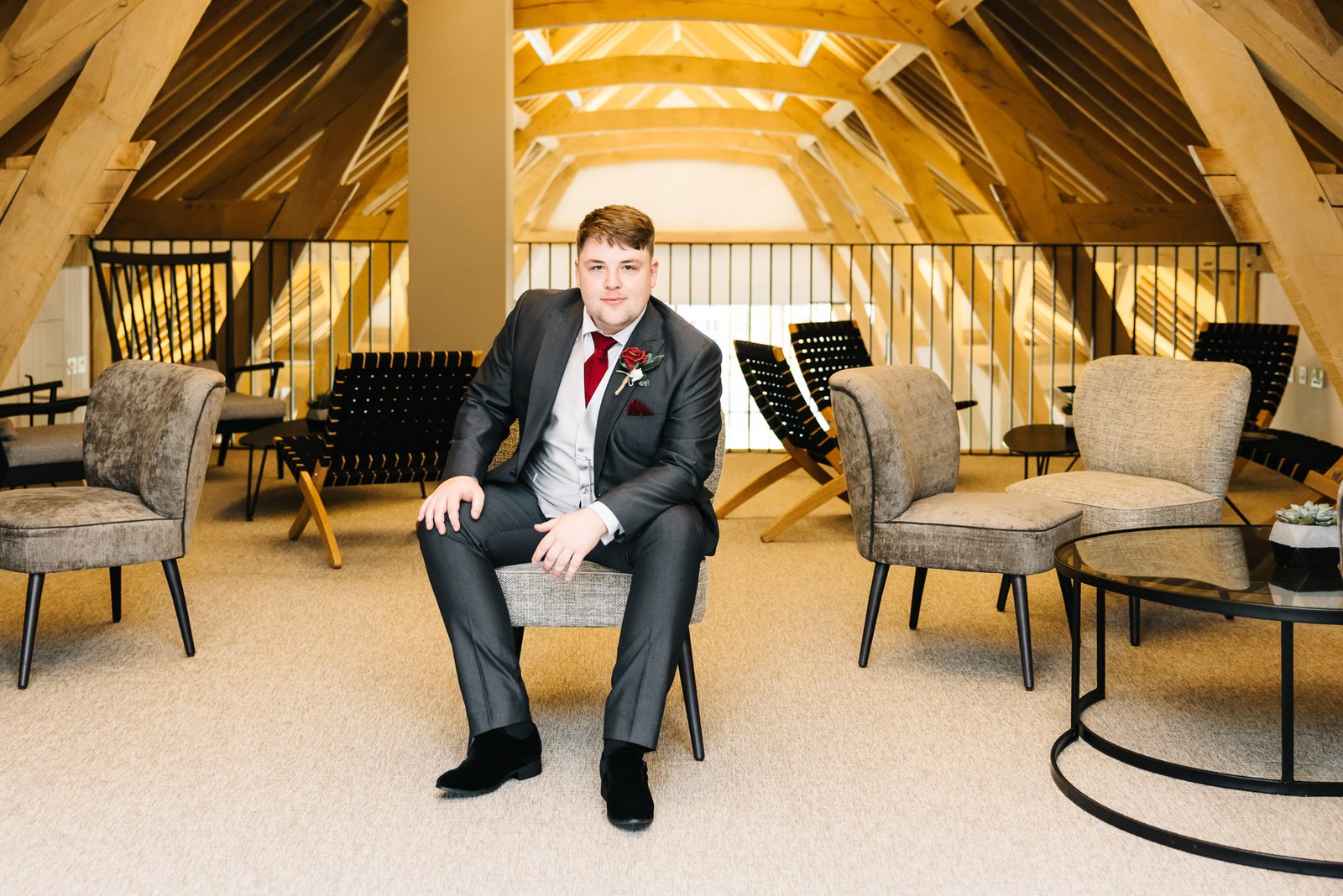 The groom sitting alone in the oak-framed lounge at The Post Barn