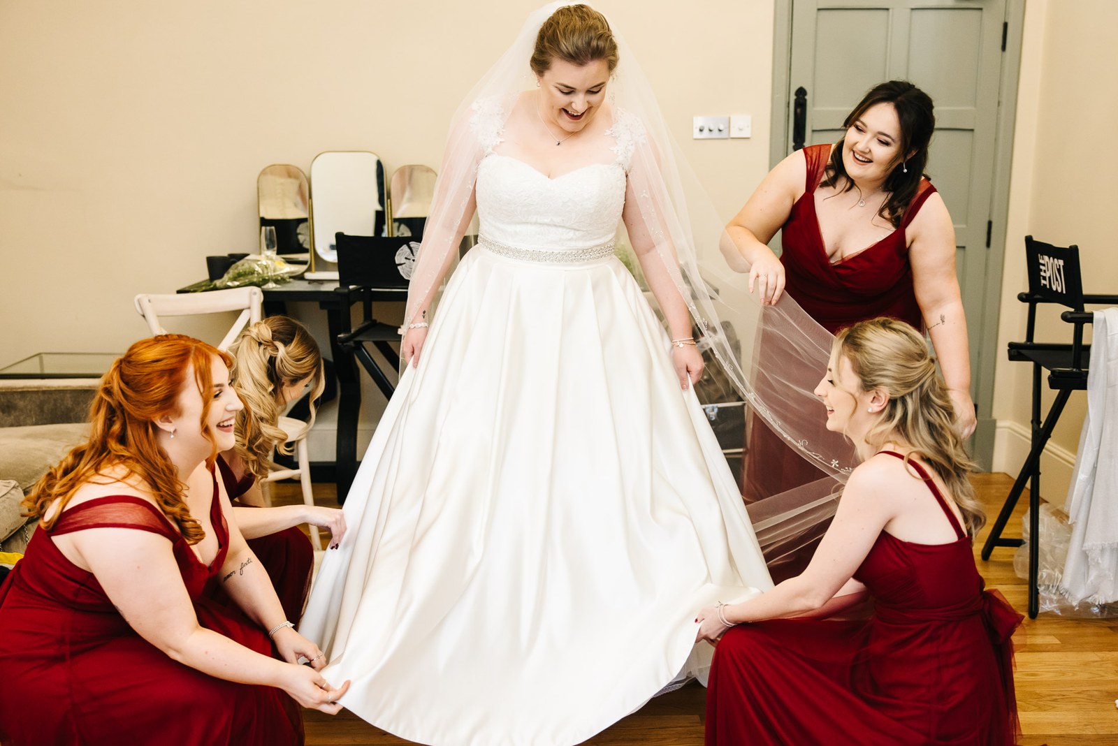 Bridesmaids in red helping the bride into her ballgown