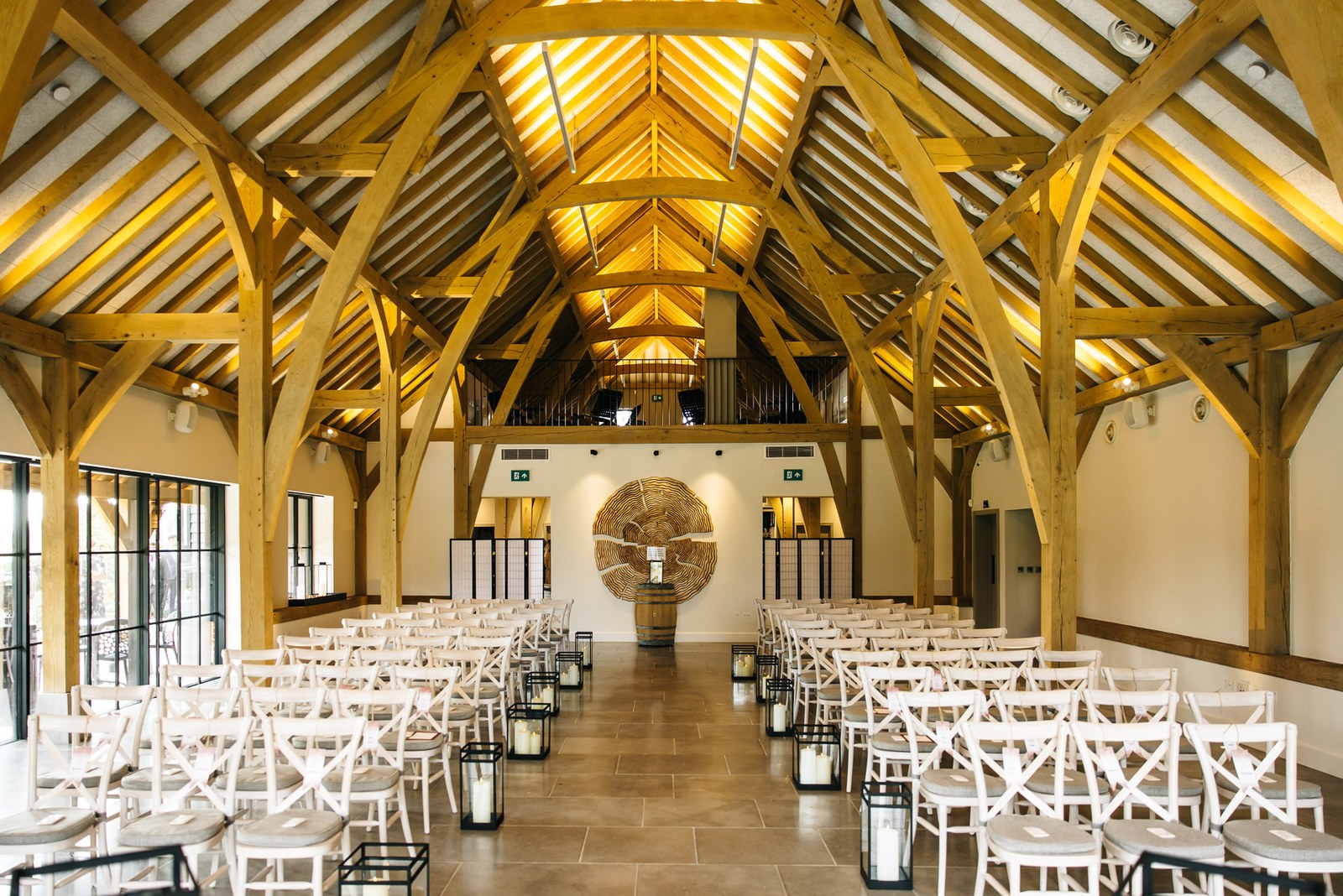 The oak-beamed ceremony barn at The Post Barn set with white chairs and lanterns