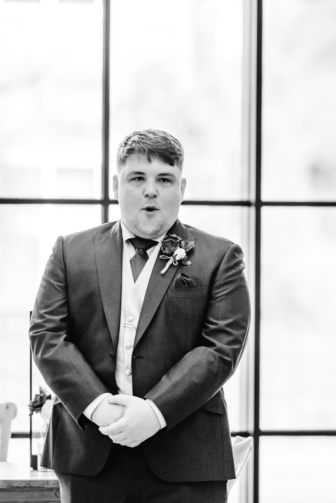 Black-and-white portrait of the groom waiting by a tall window
