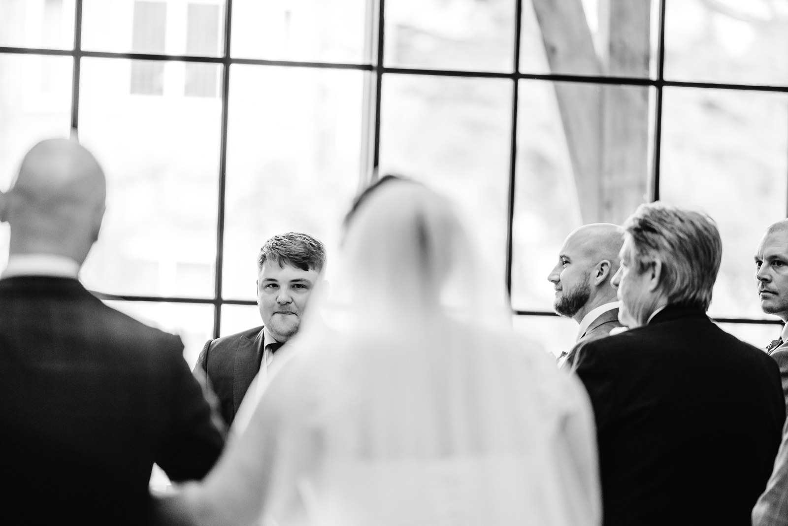 Black-and-white view of the bride facing the groom against the tall windows