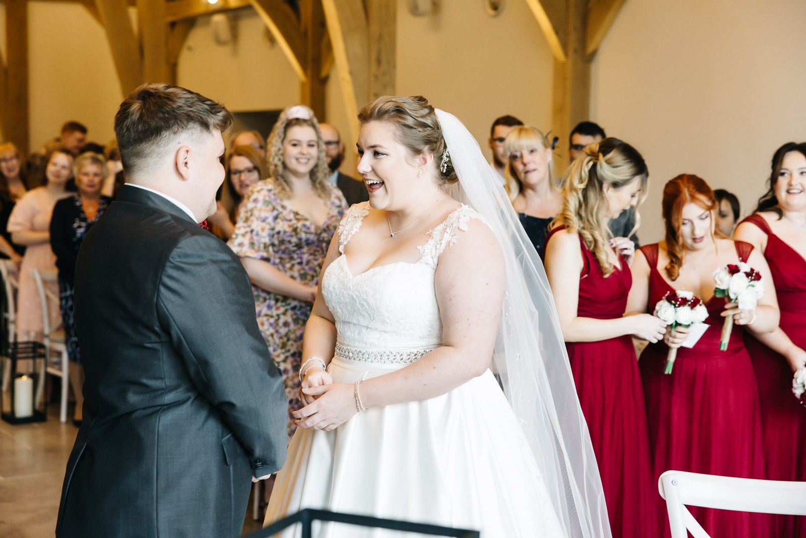 The couple facing each other at the ceremony, bridesmaids in red behind