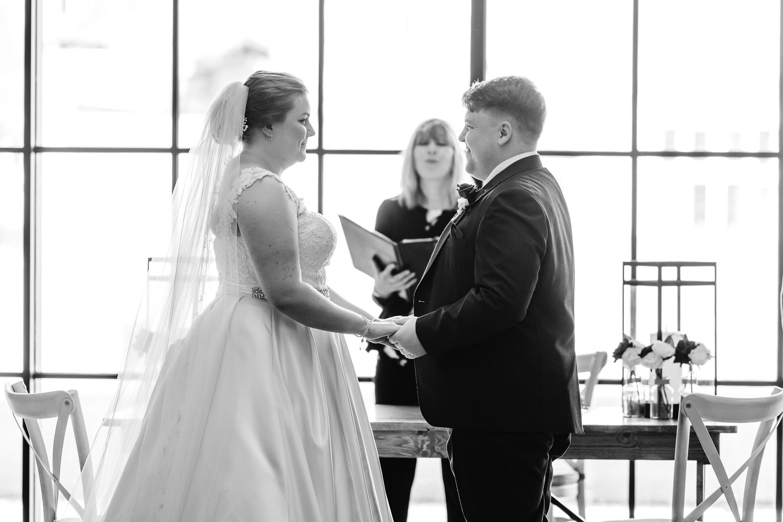 Black-and-white shot of the couple exchanging vows before the celebrant
