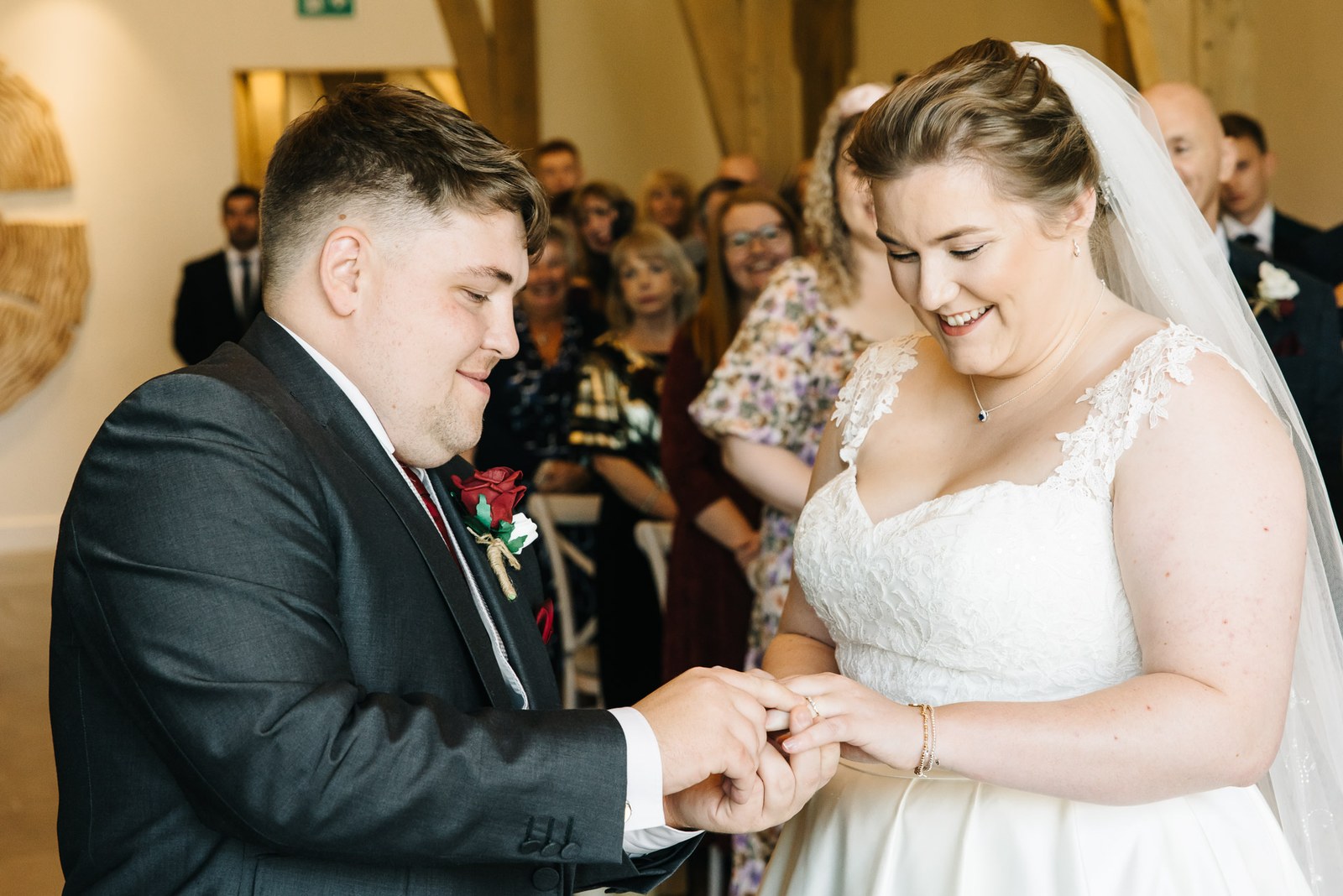 The bride sliding the ring onto the groom's finger as guests watch