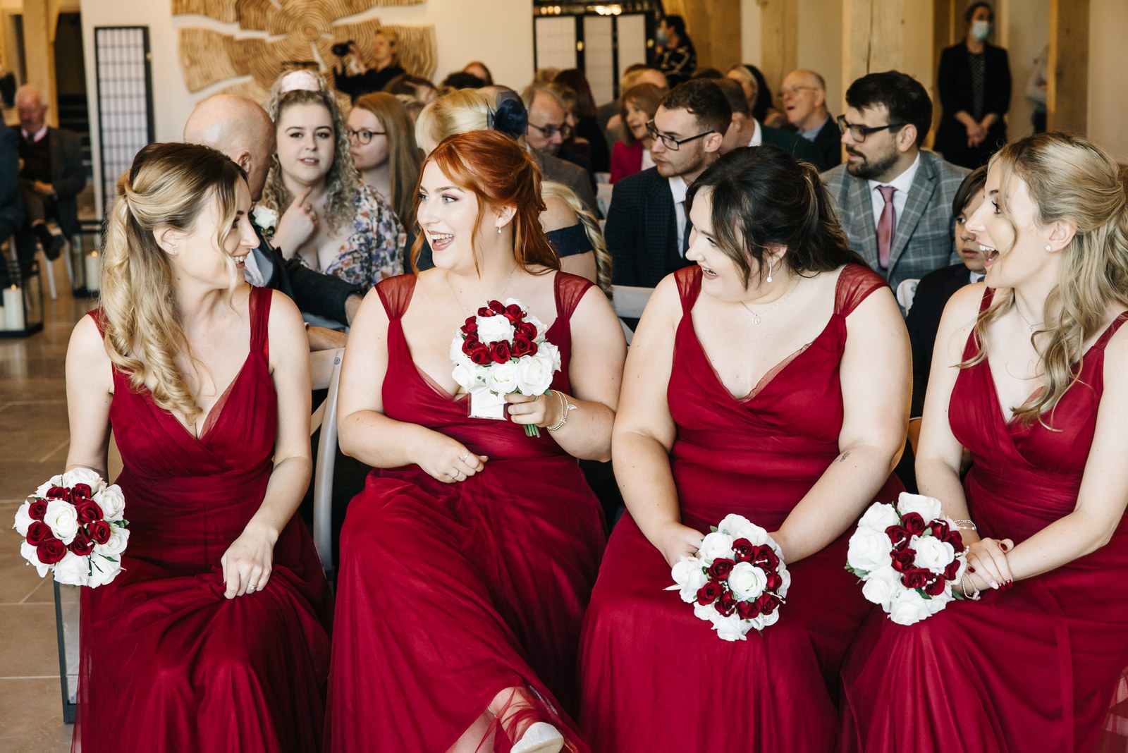 Bridesmaids in red laughing during the ceremony with their bouquets