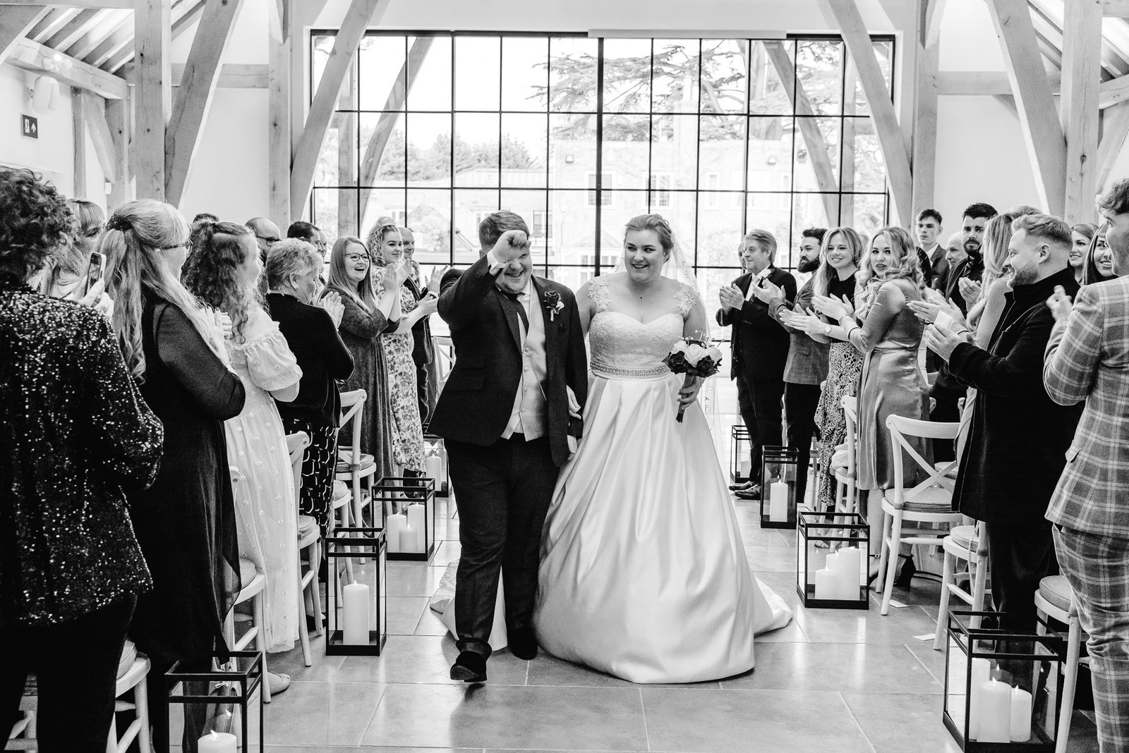 Black-and-white recessional as the couple walk back beneath the beams at The Post Barn
