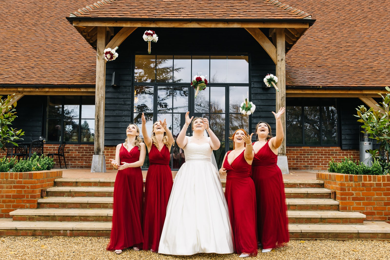 Bridesmaids in red tossing their bouquets into the air by the steps