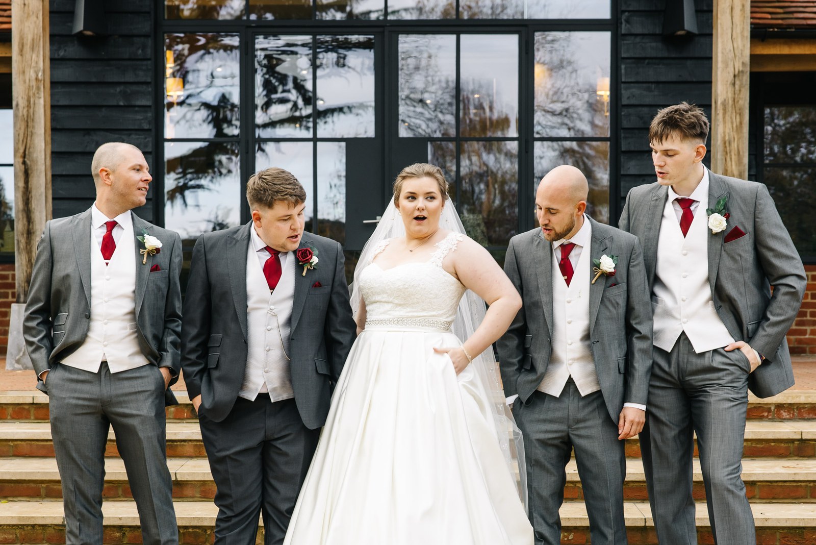 The bride with the groom and his groomsmen in grey on the steps outside The Post Barn