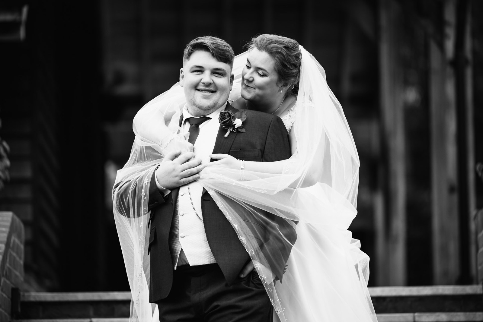 Black-and-white shot of the groom holding the bride as her veil swirls