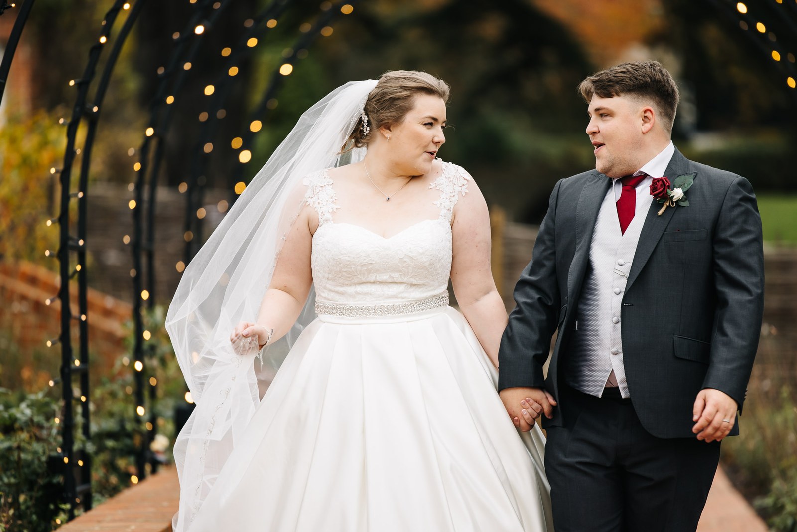 The couple under the fairy-lit garden arch, the bride's veil trailing