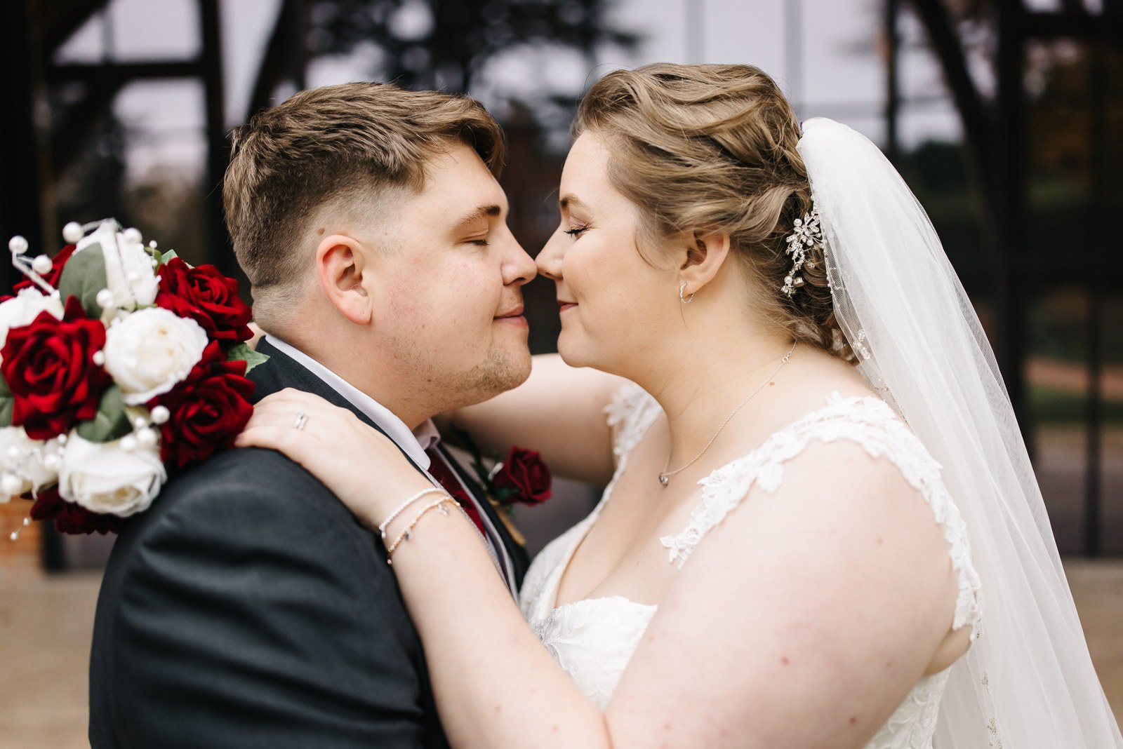 The couple nose to nose, the bride holding the red and white bouquet