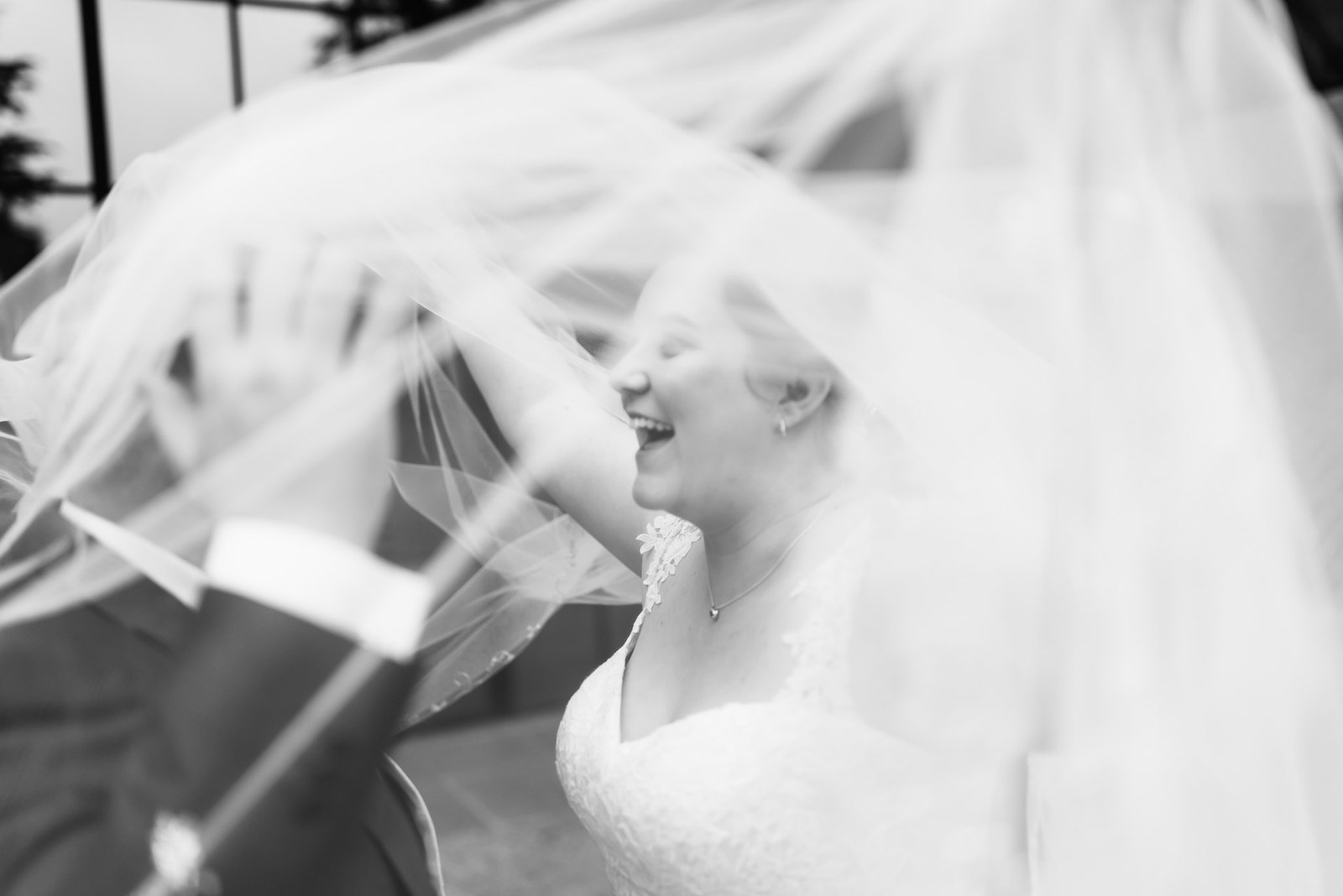 Black-and-white close-up of the bride laughing as her veil blows across