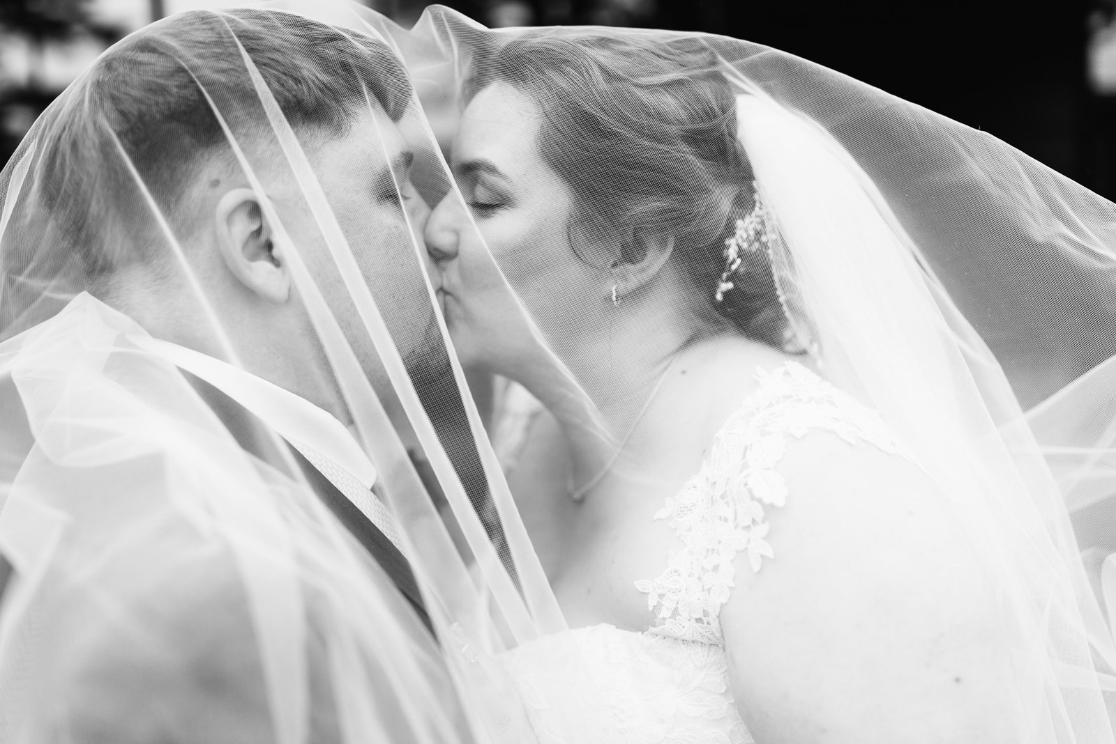 Black-and-white shot of the couple kissing beneath the billowing veil