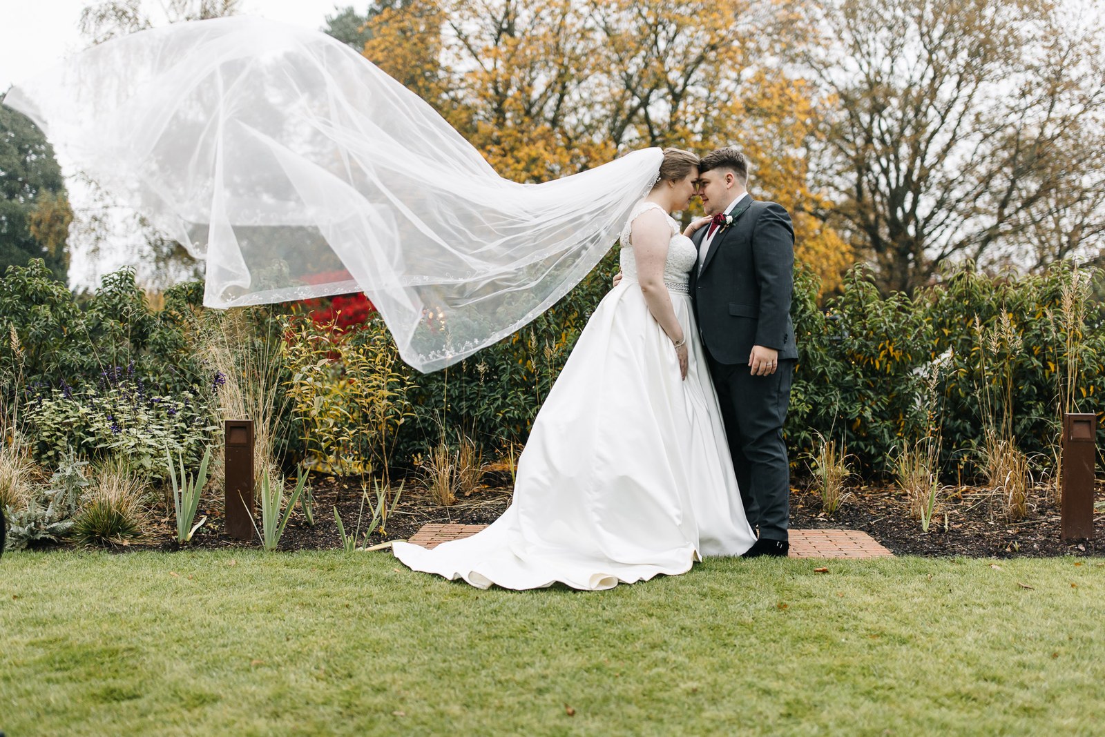 The couple in the autumn garden as the veil lifts in the wind