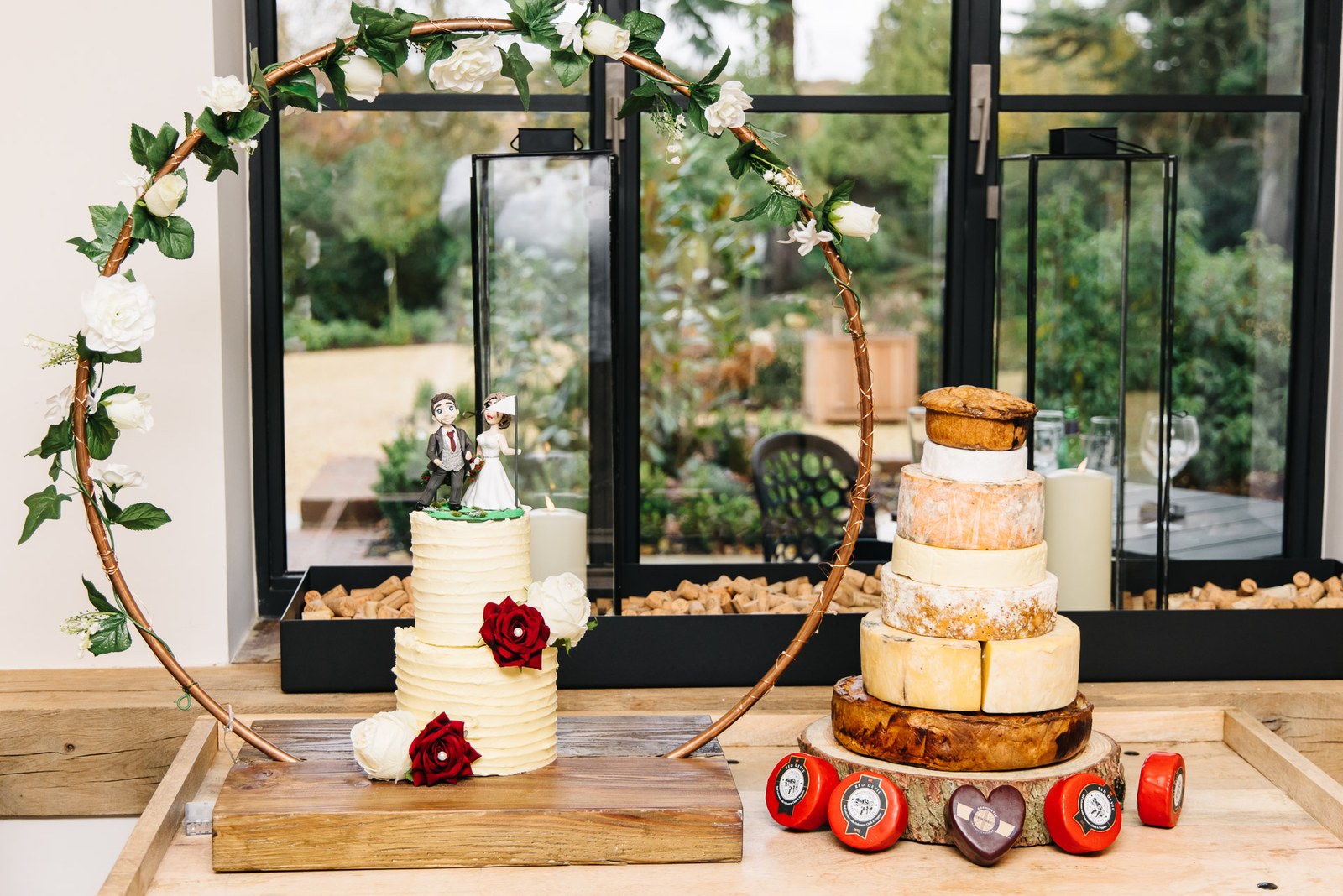 The iced wedding cake in a floral hoop beside a cheese-wheel tower at the barn window