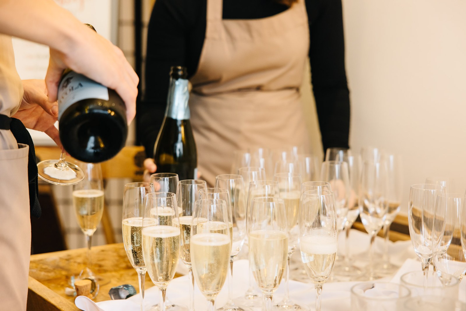 A server pouring prosecco into rows of champagne flutes