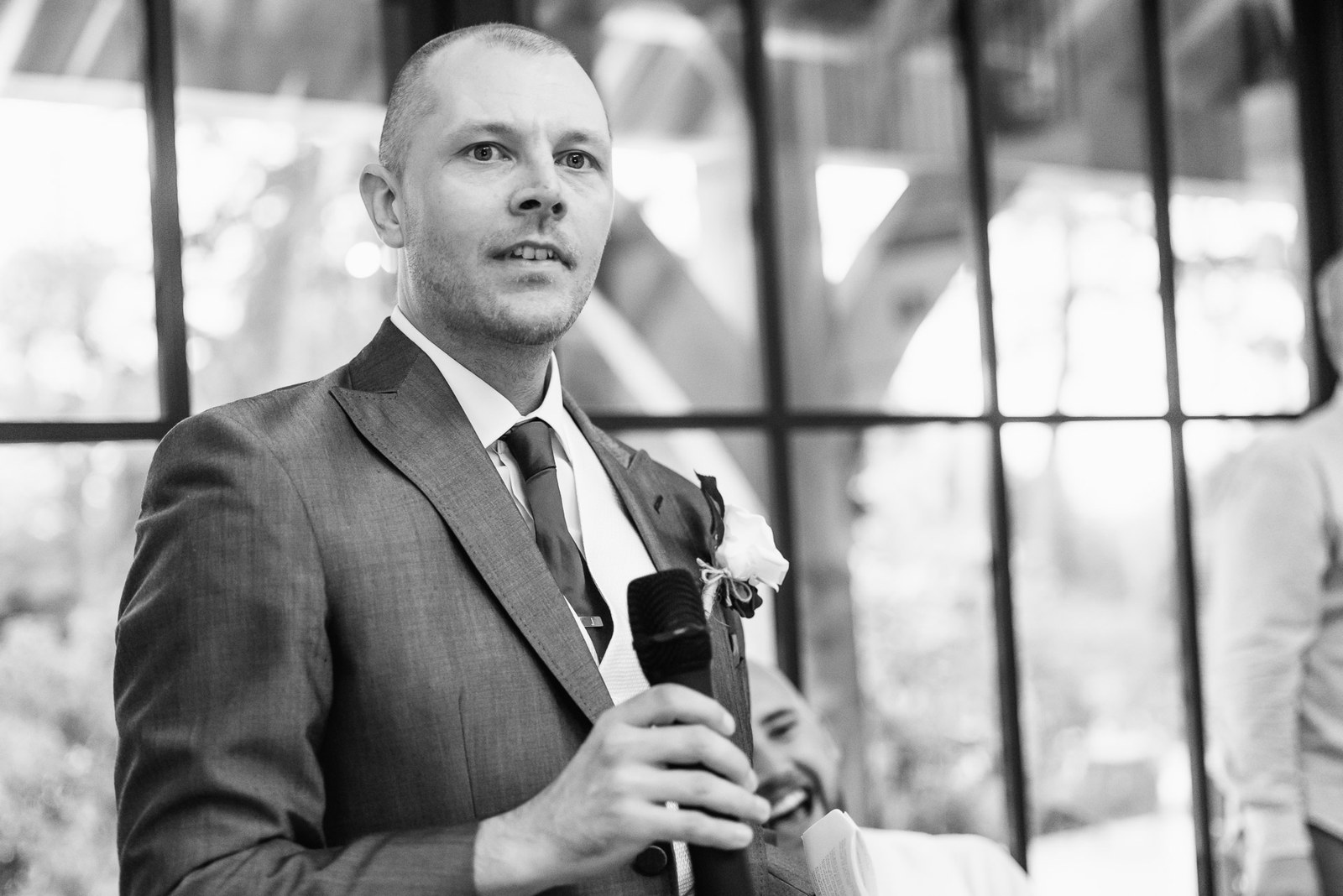 Black-and-white shot of the best man giving his speech by the window