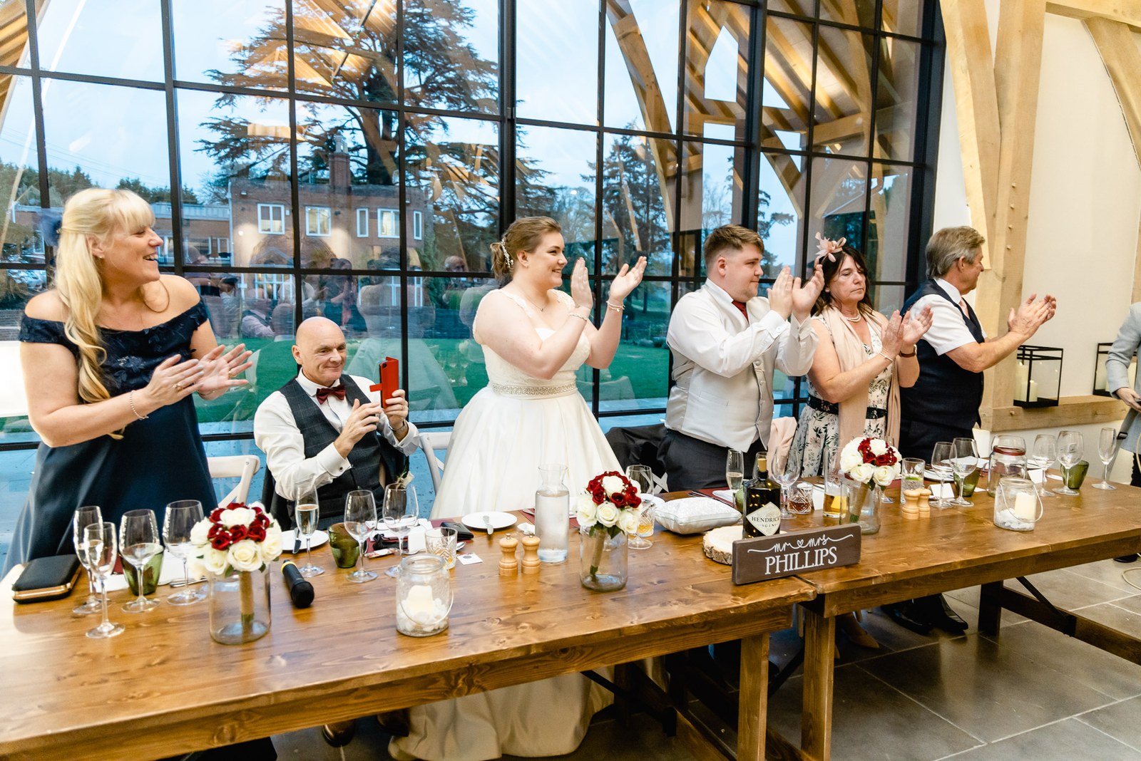 The top table applauding before the tall windows at The Post Barn