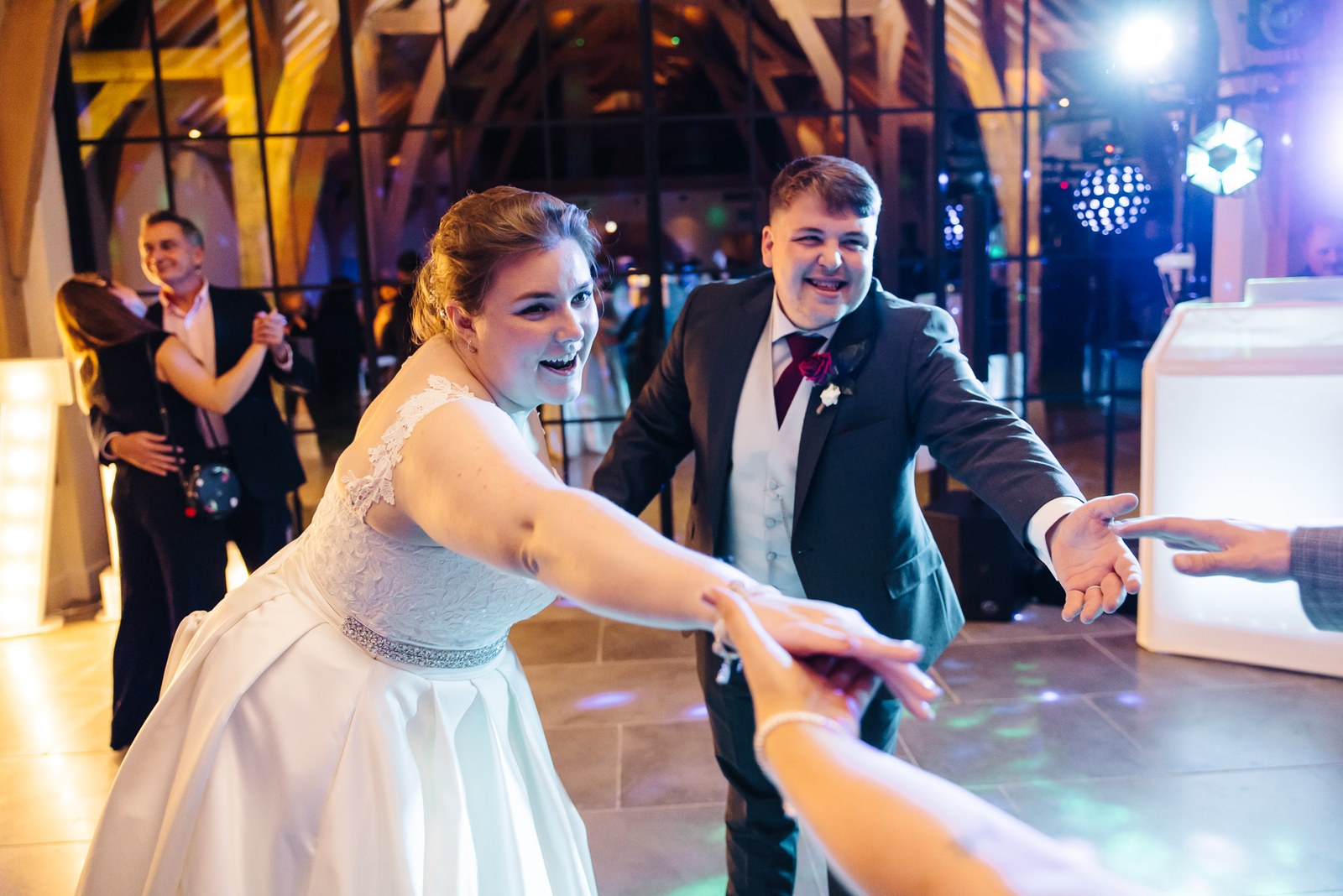 The bride pulling a guest onto the dance floor under disco lights