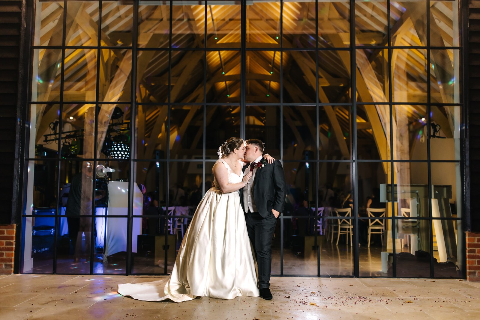 The couple kissing on the dance floor framed by the tall barn windows