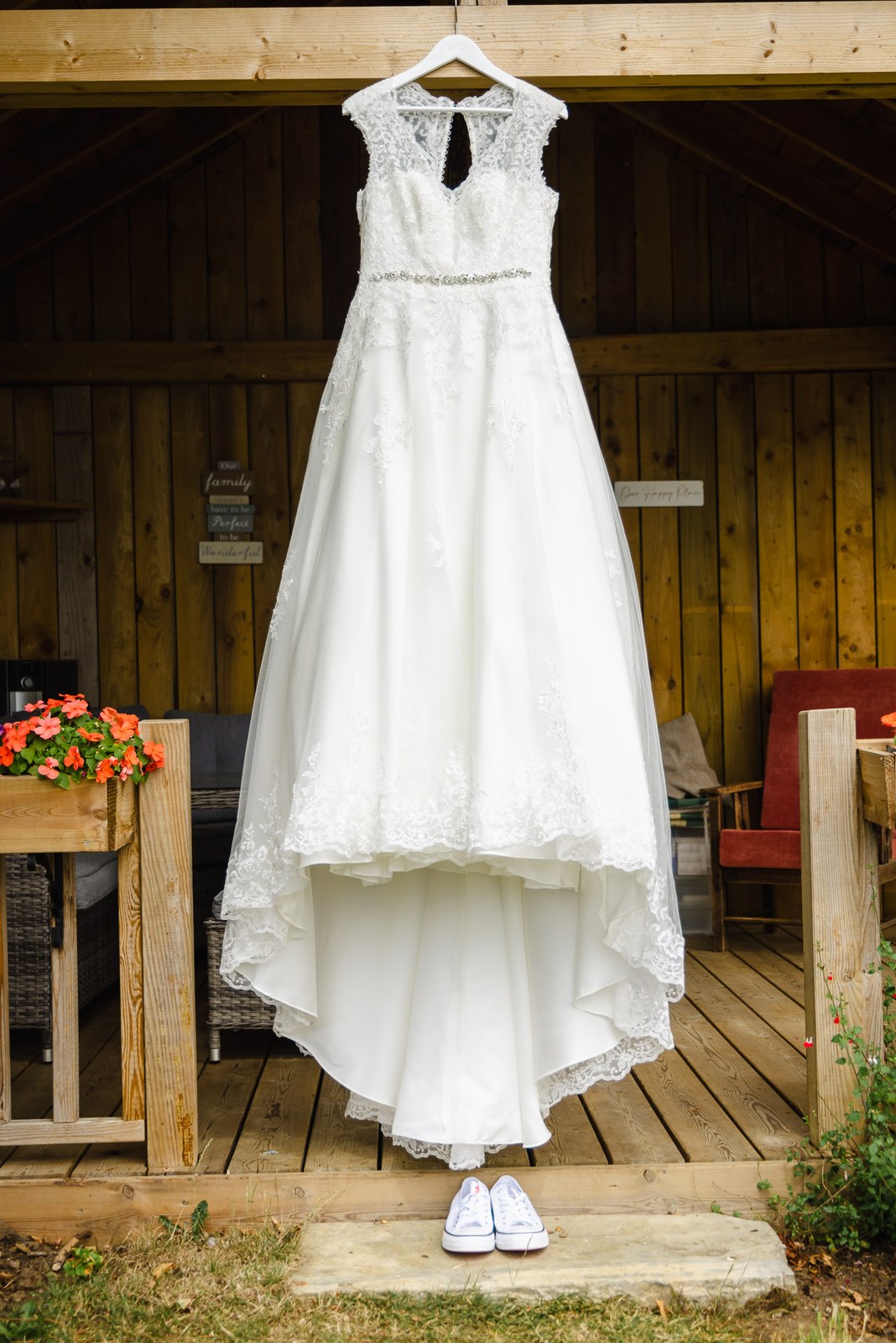Lace wedding gown hanging on the timber-clad barn wall at Slapton Manor, trainers below