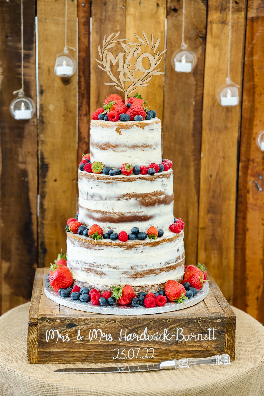 Semi-naked tiered wedding cake topped with berries on a rustic crate against reclaimed wood